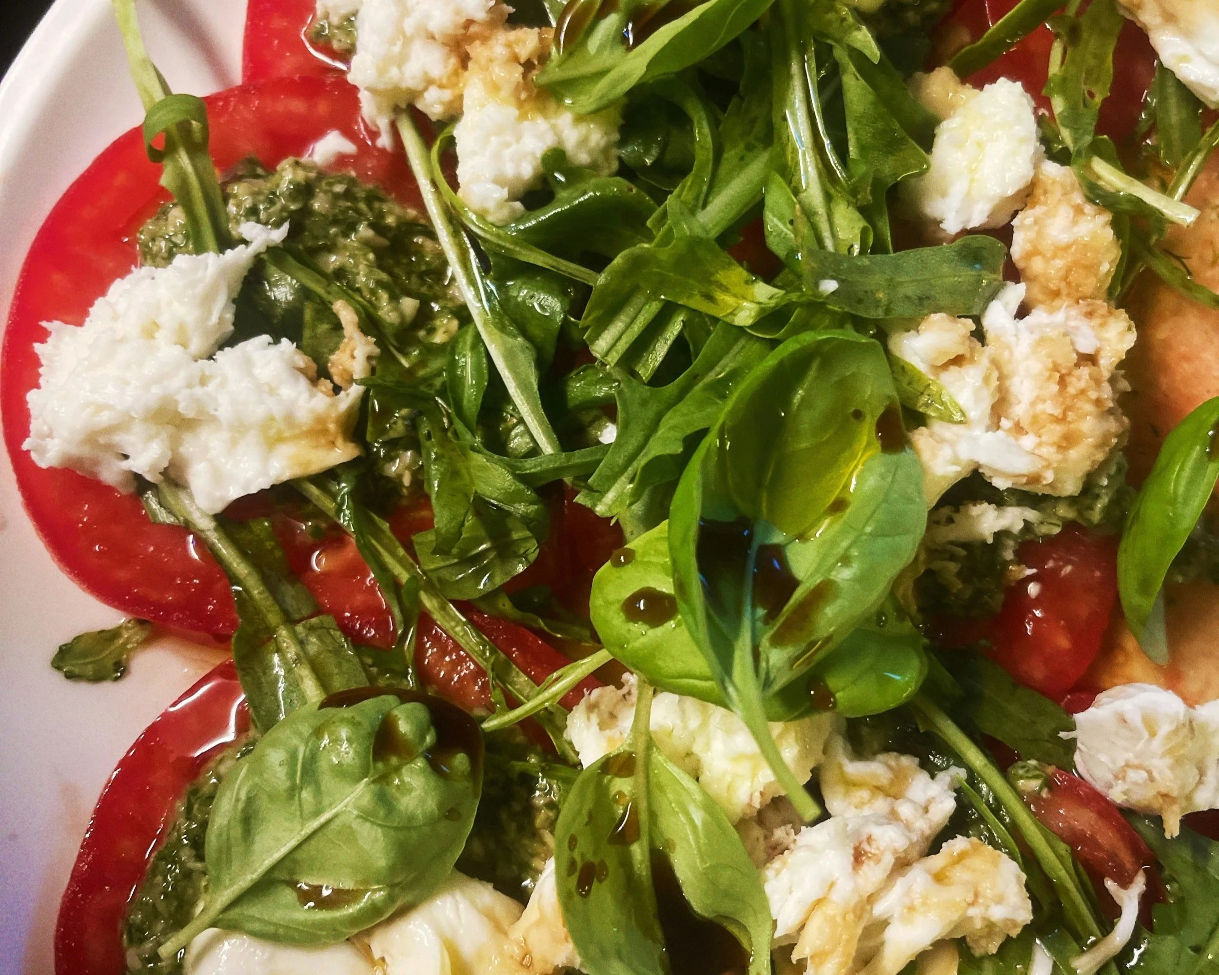 A plate of salad with fresh green leafy vegetables, sliced tomatoes, and crumbled cheese.