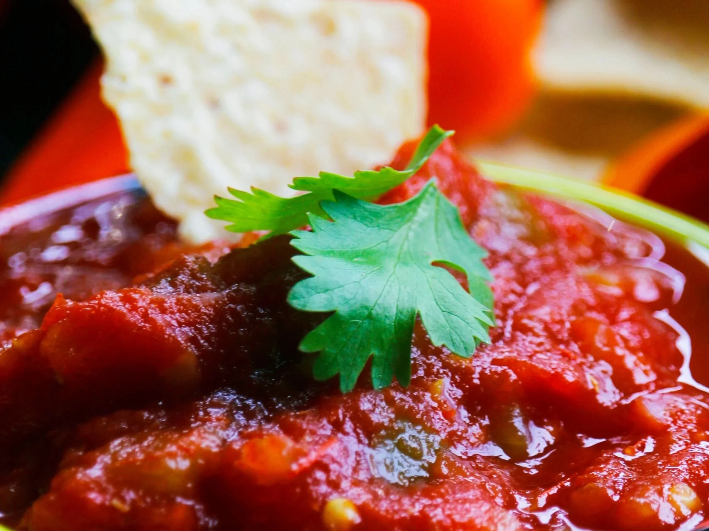 Close-up of a dish of seasoned ground meat topped with fresh cilantro and red sauce.