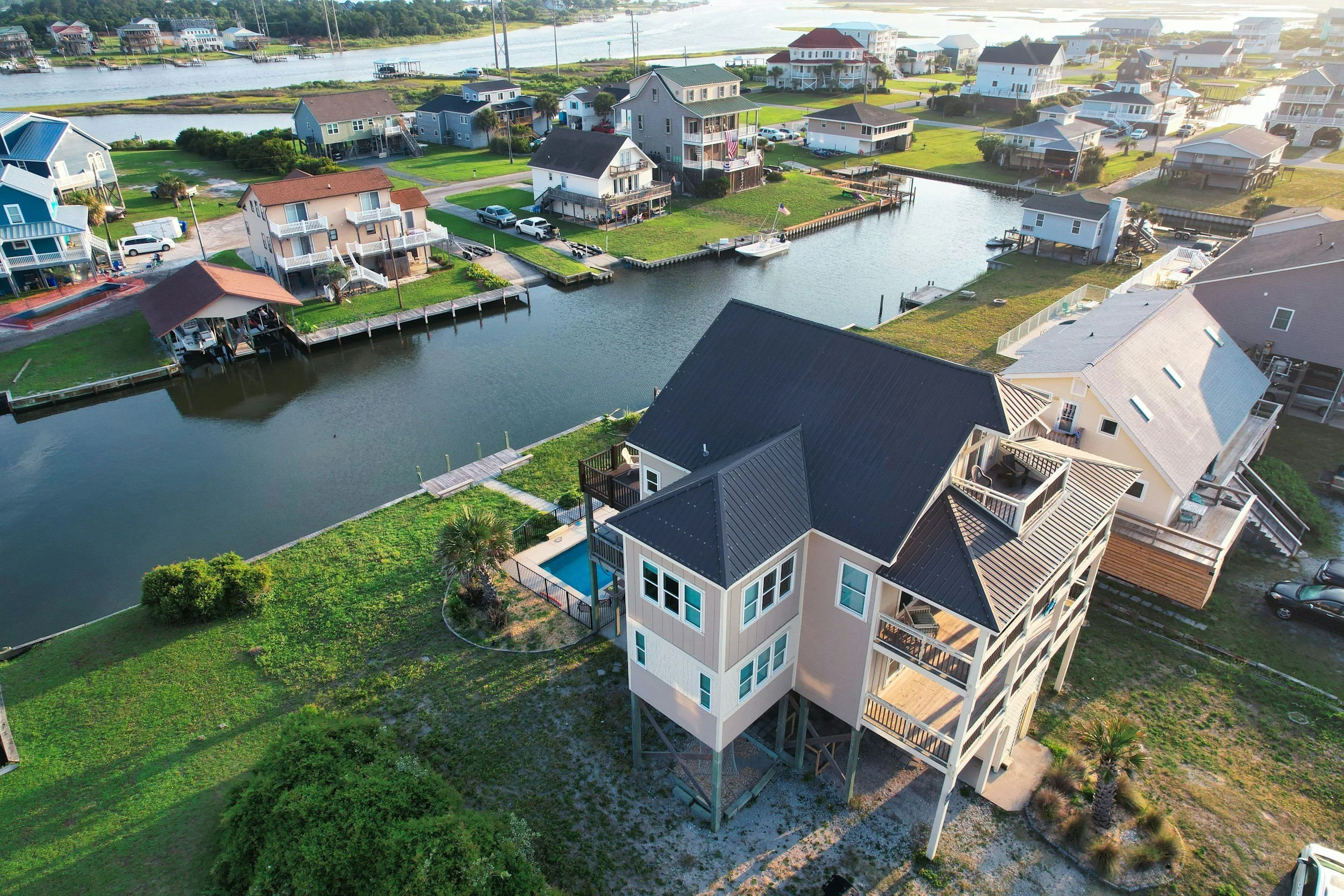 Aerial view of a neighborhood near a waterway with houses on stilts, docks, boats, and lush greenery.