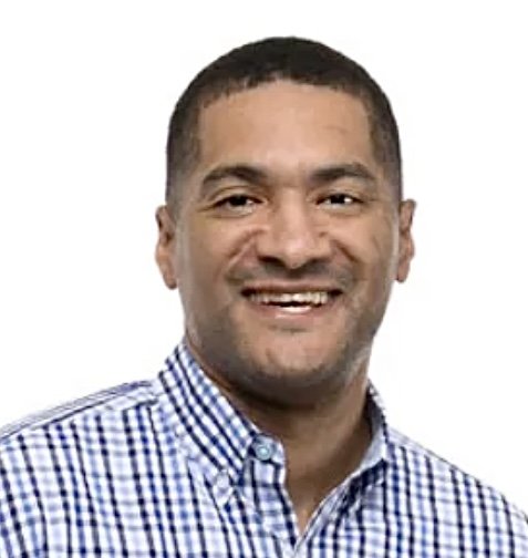 Smiling man with short dark hair, wearing a blue and white checkered shirt, against a plain white background.