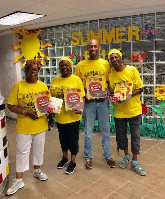 Four people wearing yellow shirts holding books in a decorated room with the word 'SUMMER' on the wall.
