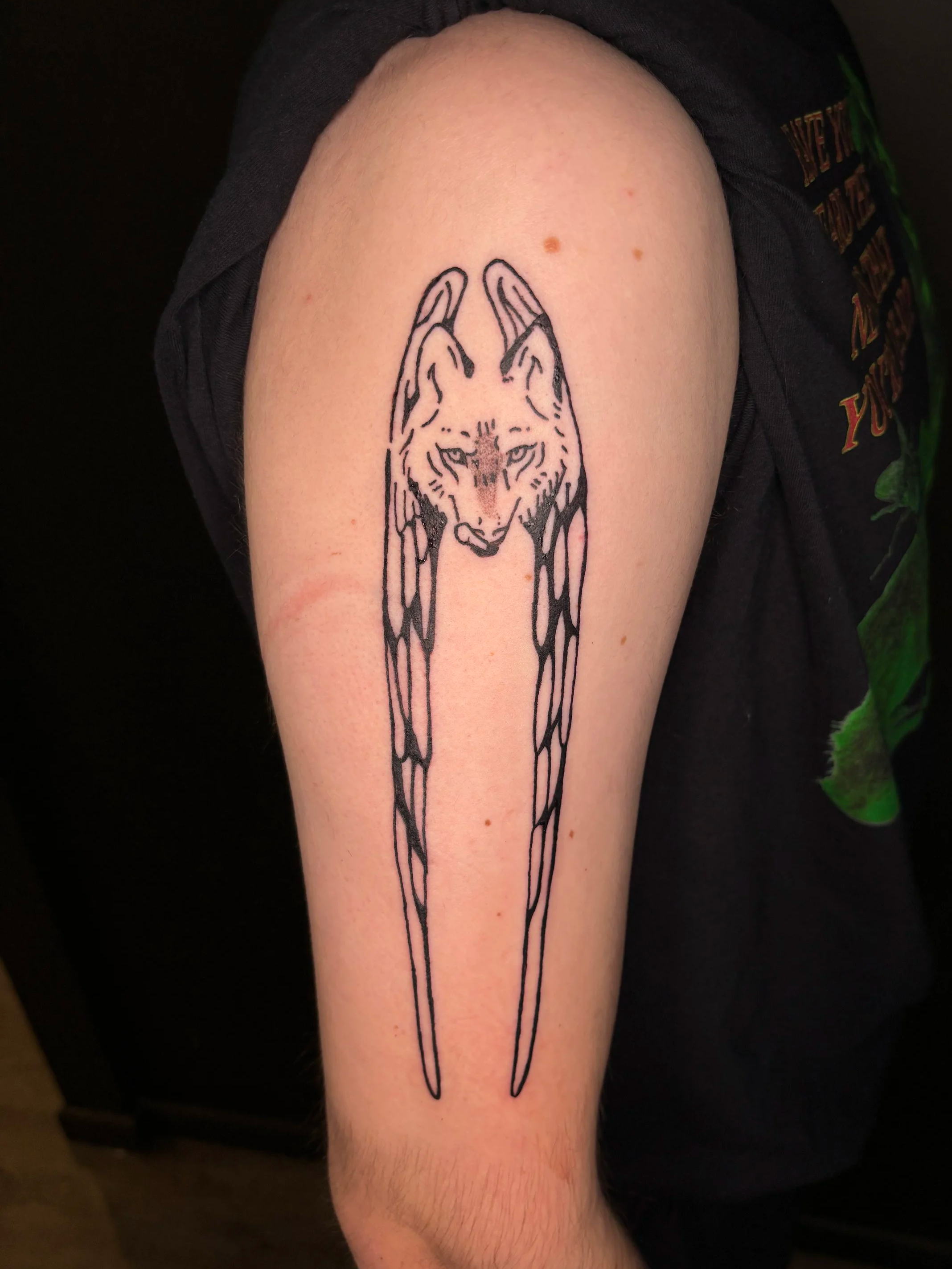 A tattoo of a wolf's head with long, flowing lines extending downward on a person's upper arm.