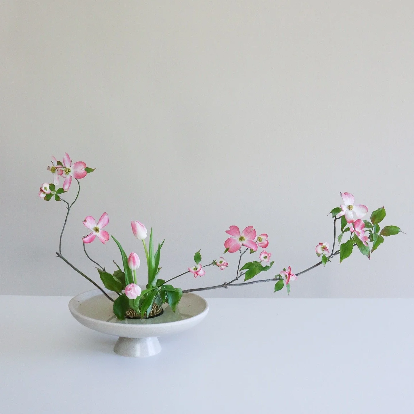 Pink and white artificial flower arrangement in a white ceramic bowl on a white surface against a light gray wall.