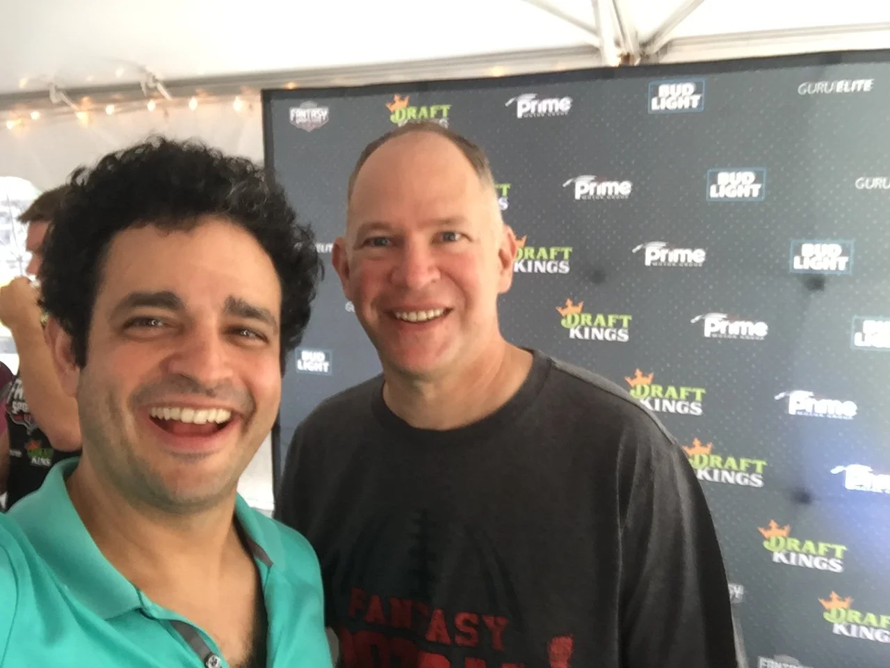 Two smiling men taking a selfie at an event with a backdrop displaying logos for DraftKings, Prime, Bud Light, and Guru life.