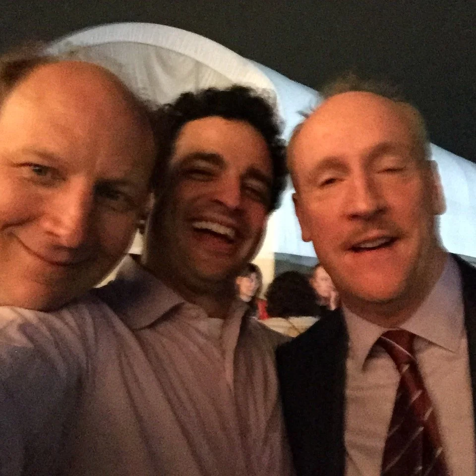 Three men are taking a selfie together, smiling and appearing happy at a social event or gathering.