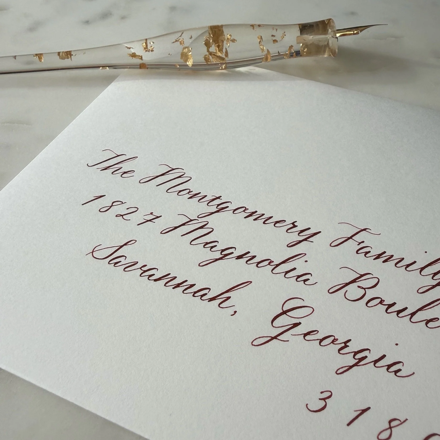 Envelope hand-addressed in dark cranberry red calligraphy, with a pointed pen in the background