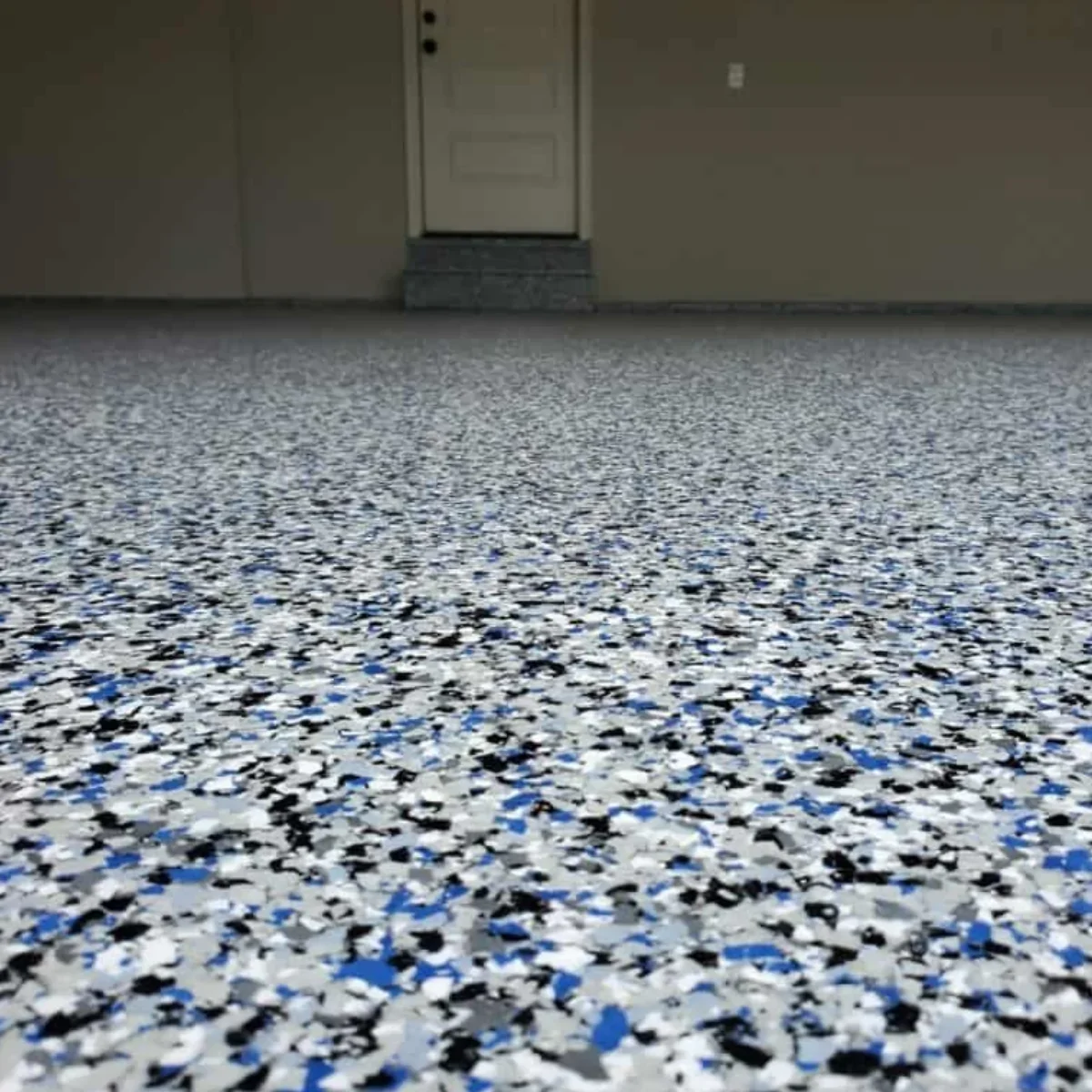 Close-up of a speckled epoxy floor with gray, black, white, and blue flecks, leading to a door on an interior or garage space.
