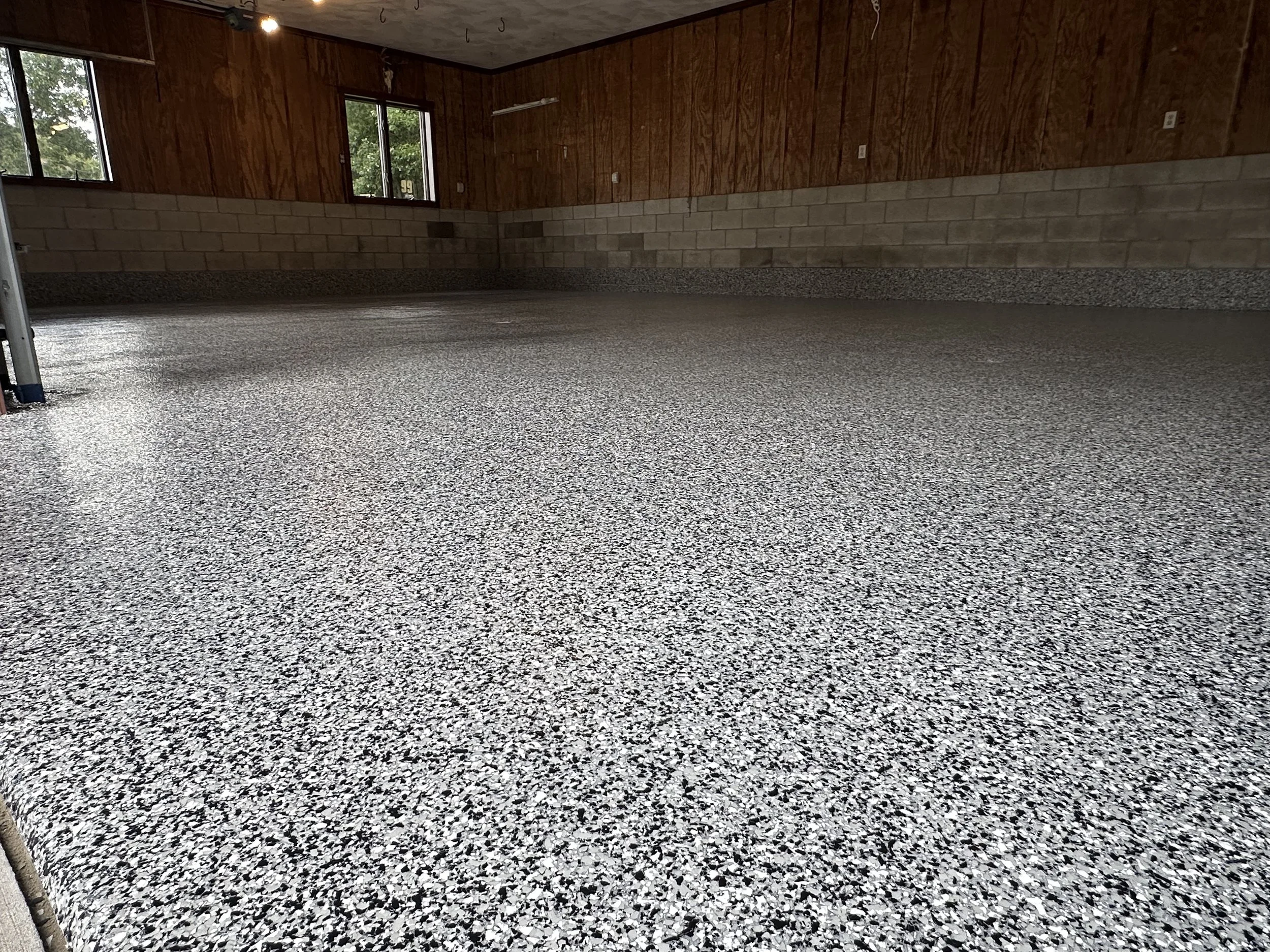 Empty garage with carpeted floor, wooden paneled walls, and windows showing greenery outside.