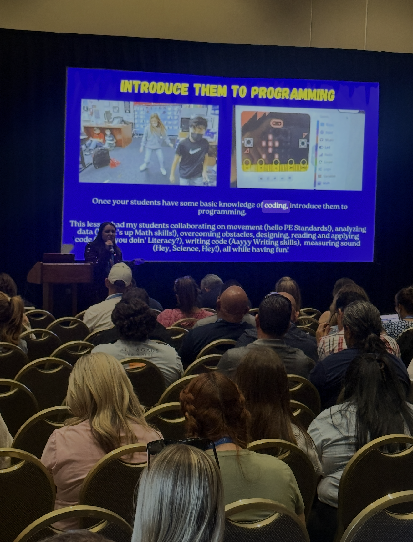 Lisa Moe presenting to a full room of educators, with a slide titled "Introduce them to programming" showing students coding a micro:bit.