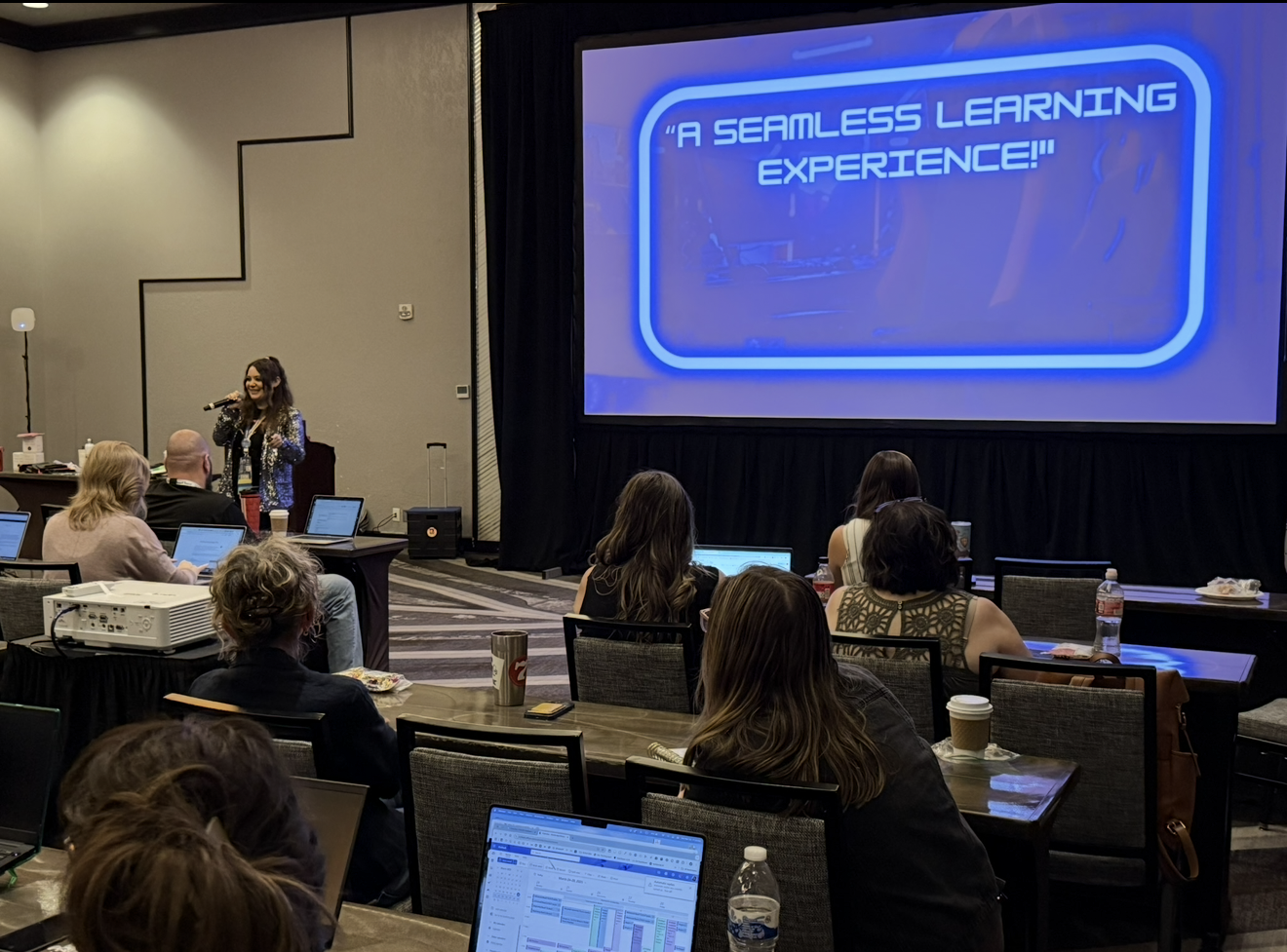 Lisa Moe leading a professional learning session for educators on laptops, beside a large screen reading A Seamless Learning Experience