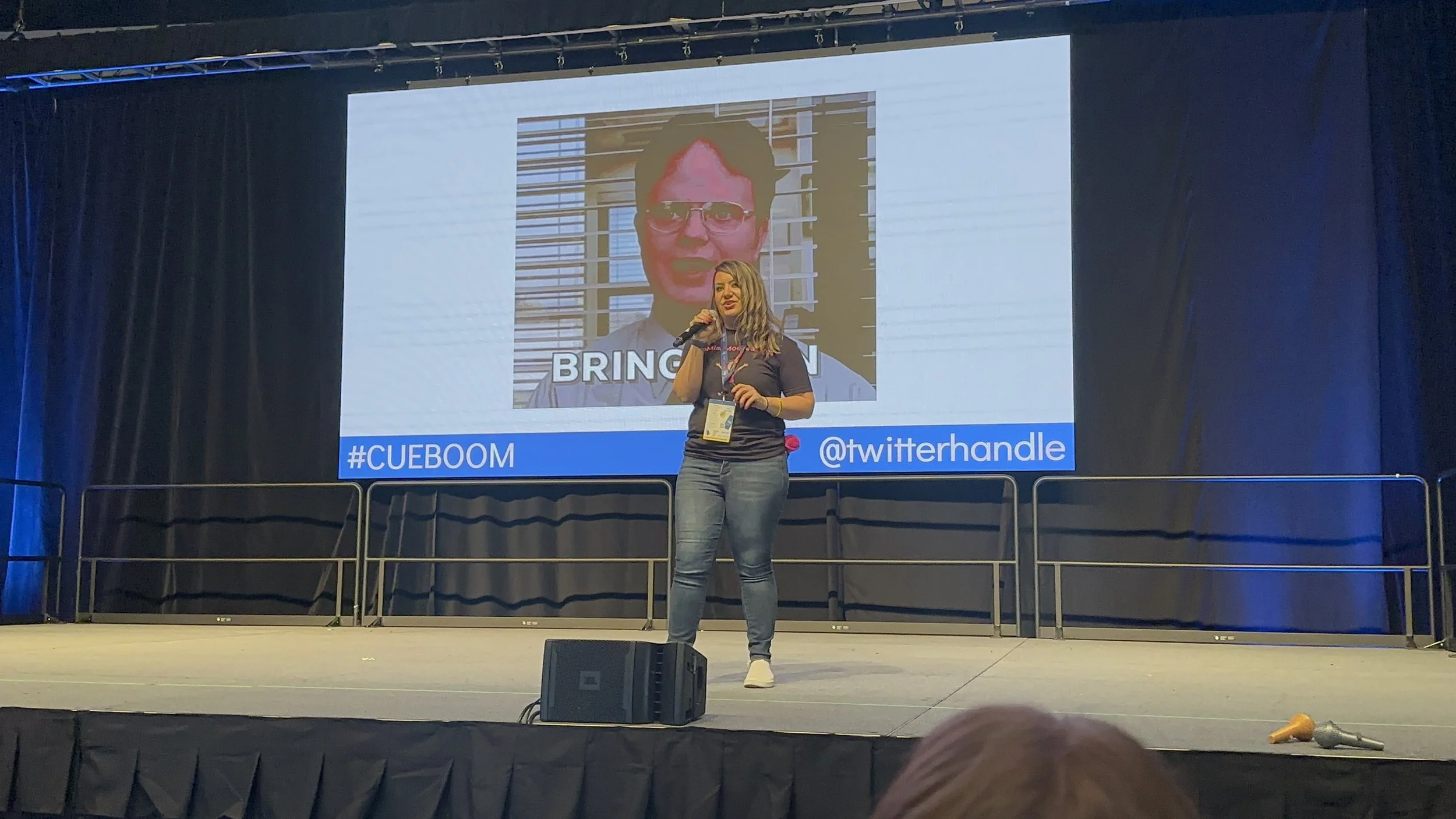 Lisa Moe on stage with a microphone at a CUE conference, in front of a big screen with a "Bring it on" slide.