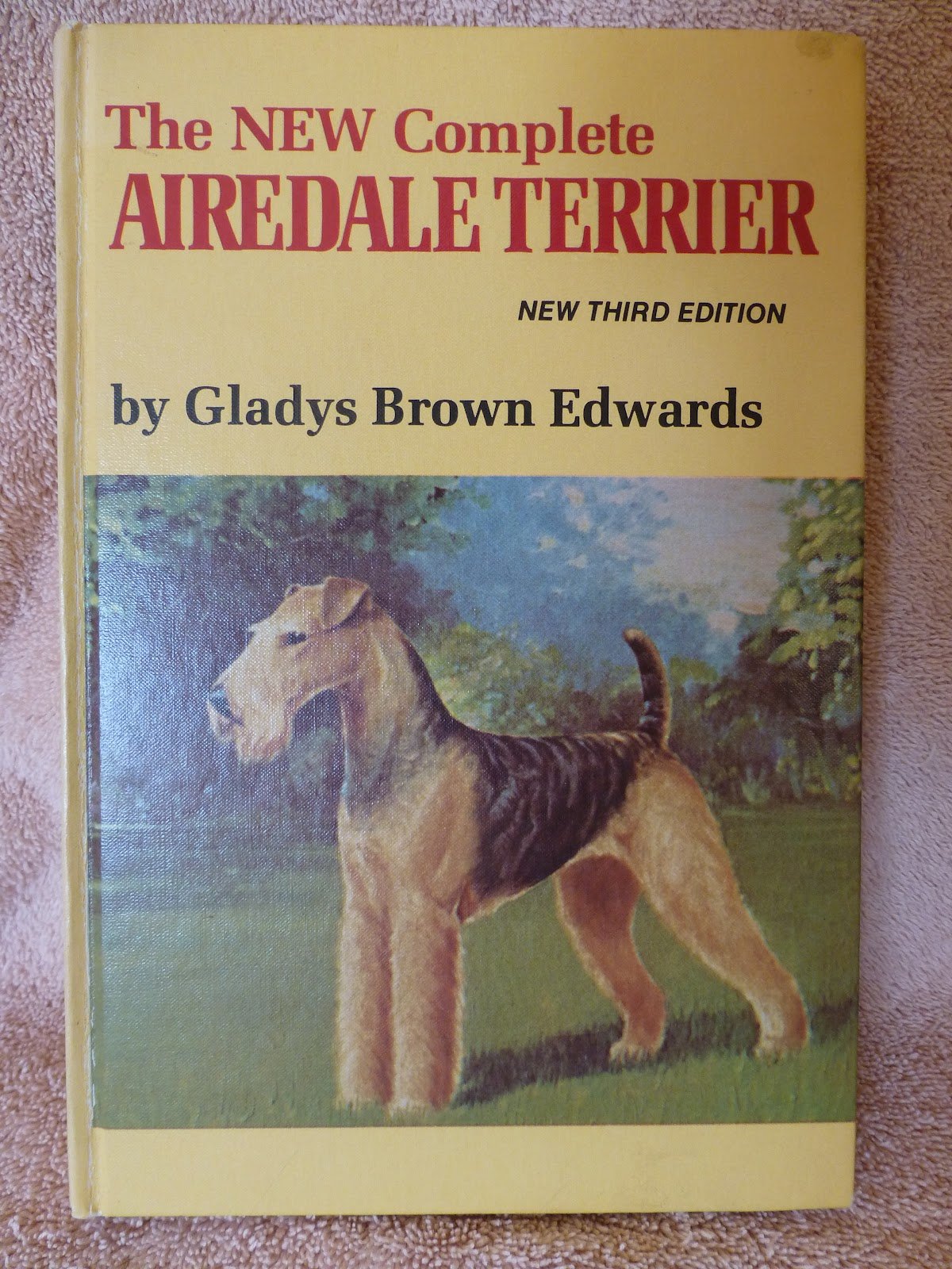 A book titled "The New Complete Airedale Terrier" by Gladys Brown Edwards, third edition, with an illustrated Airedale Terrier dog standing outdoors against a background of trees and sky.