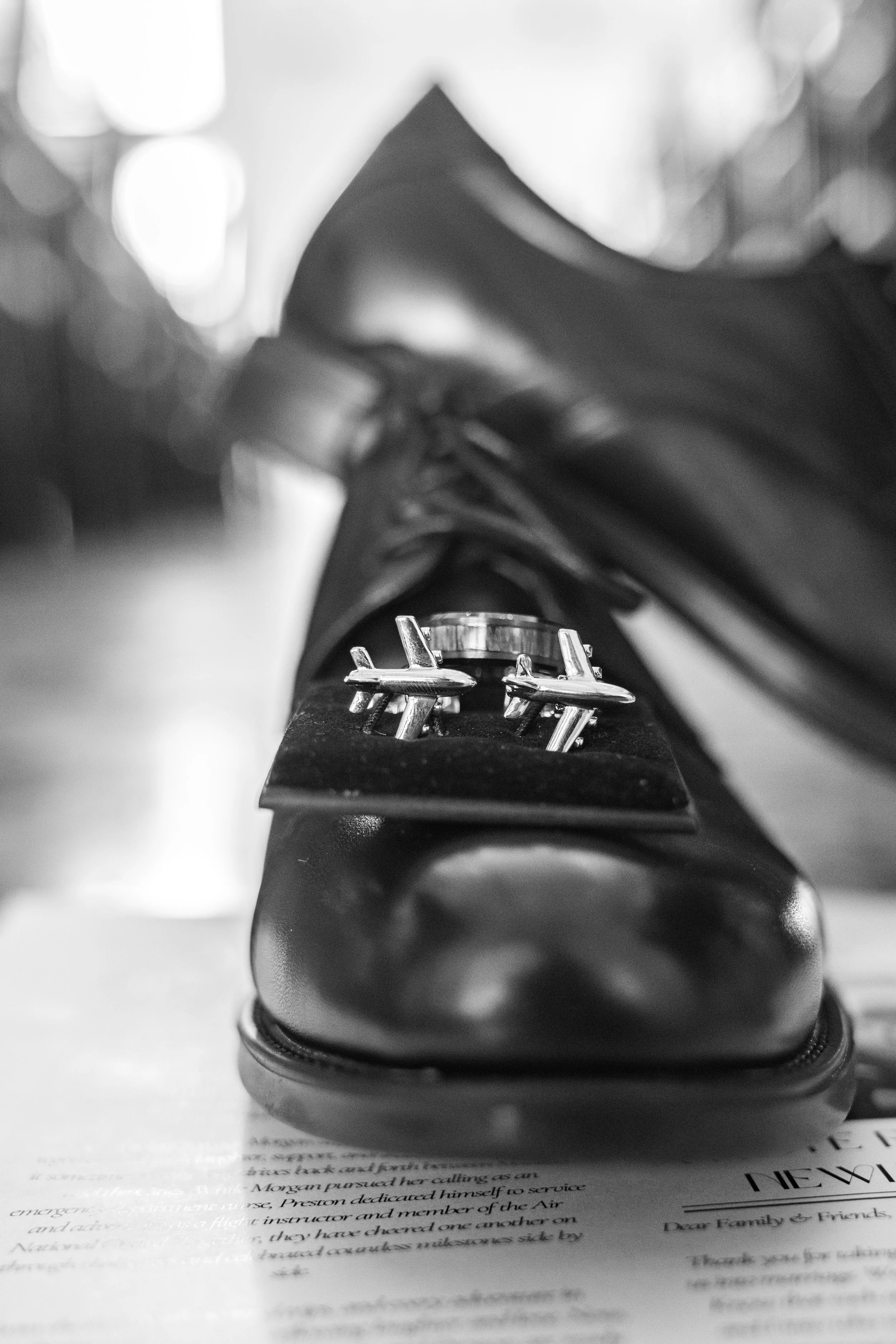 Close-up black-and-white photograph of a shoe on a piece of paper with printed text, with the focus on the shoe's sole and laces.