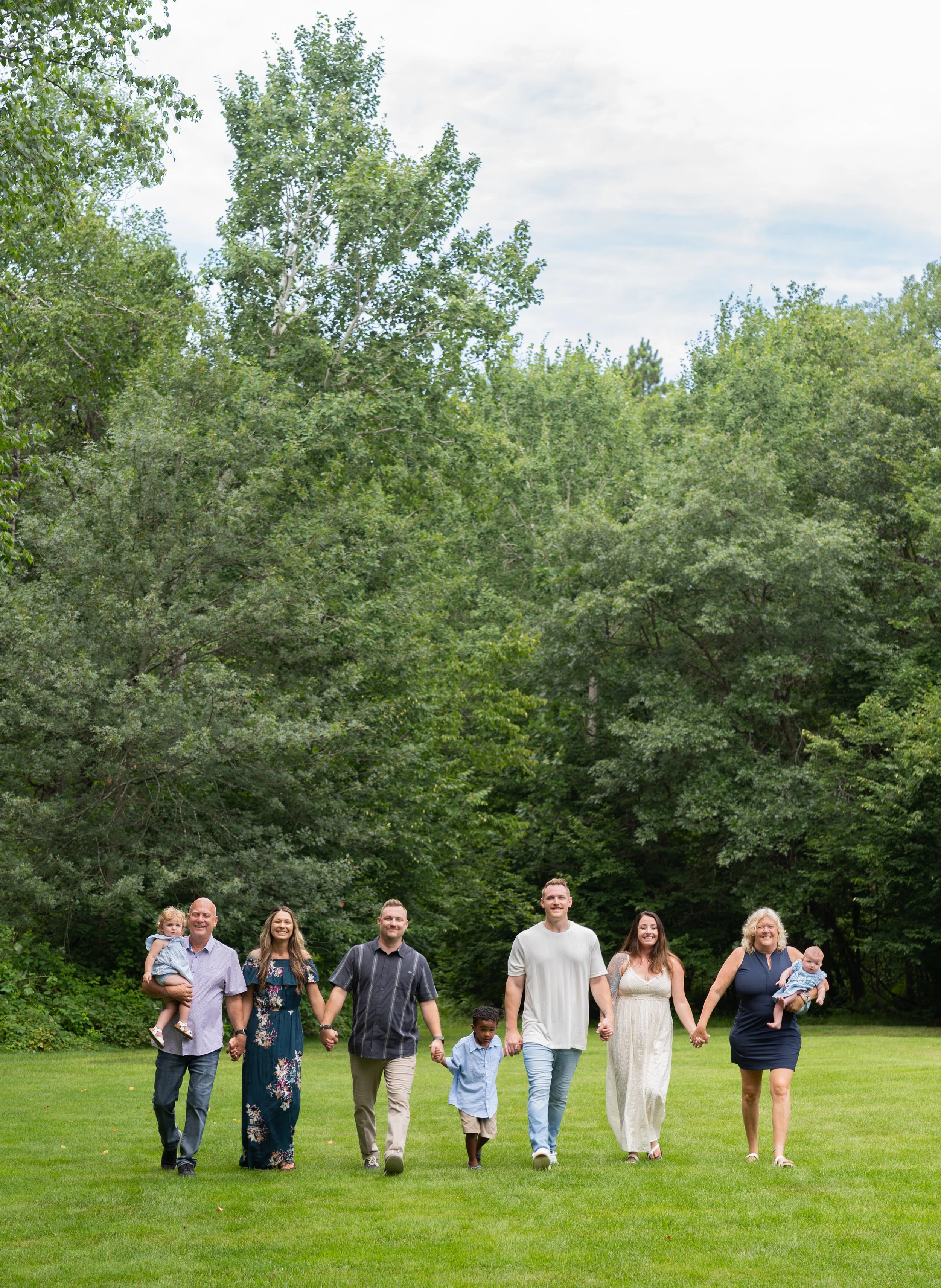 A group of people walking on a grassy field with tall green trees in the background.
