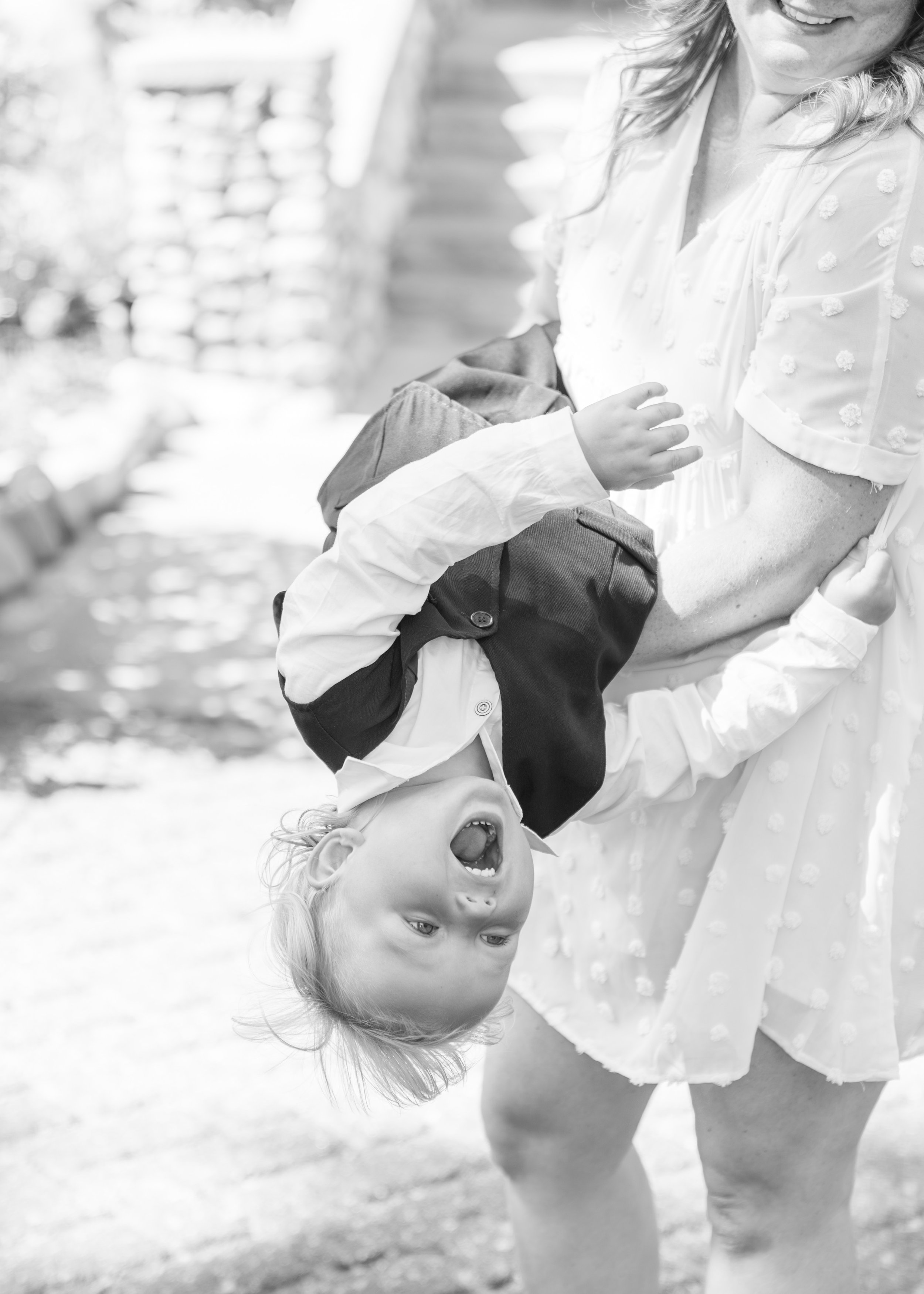 A woman in a light dress holding a laughing young girl upside down outdoors.