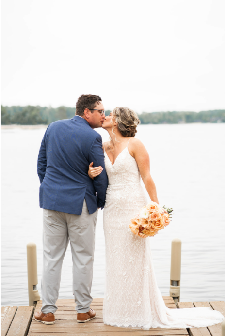 Bride and groom sharing a kiss by the water on a dock, bride holding a bouquet of flowers.