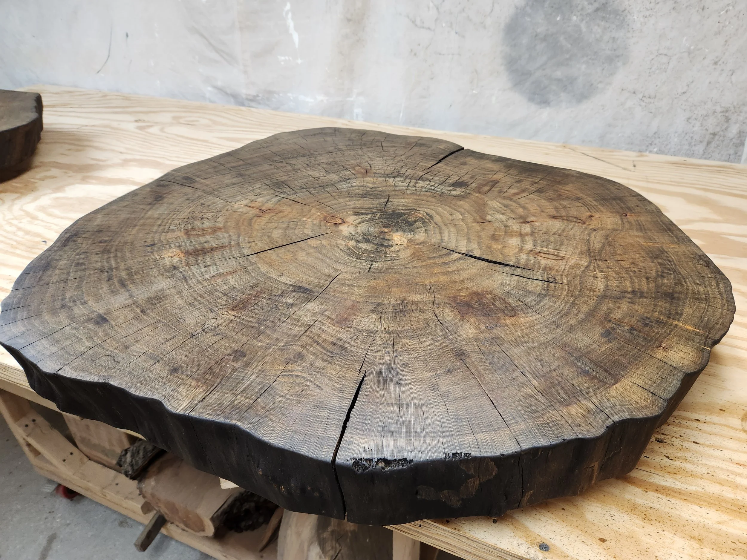 A large, round, thick wooden table with visible wood grain and cracks in the surface, on a wooden stand in our storage space.