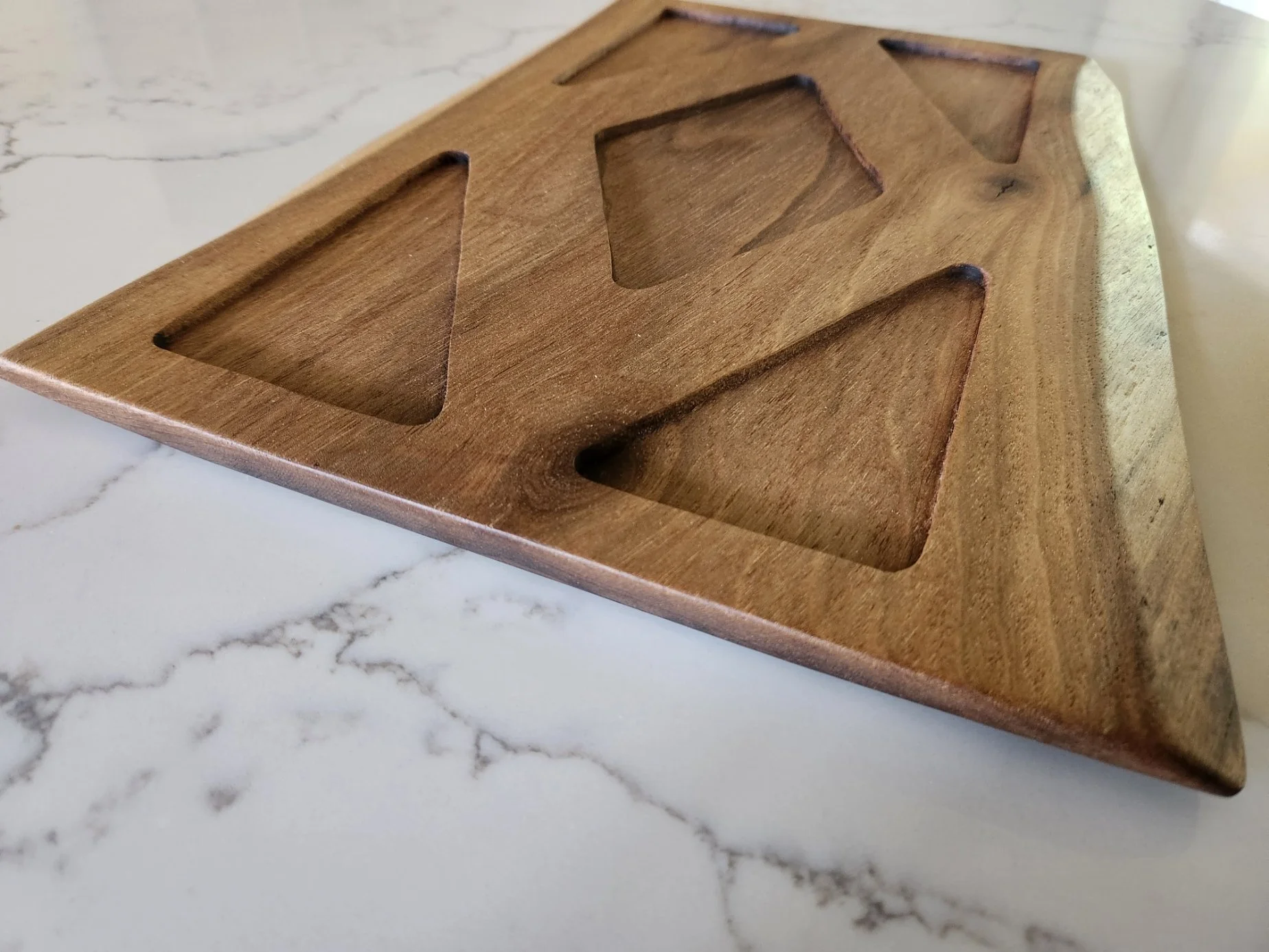 A wooden tray with carved compartments is placed on a white marble surface with gray veining.