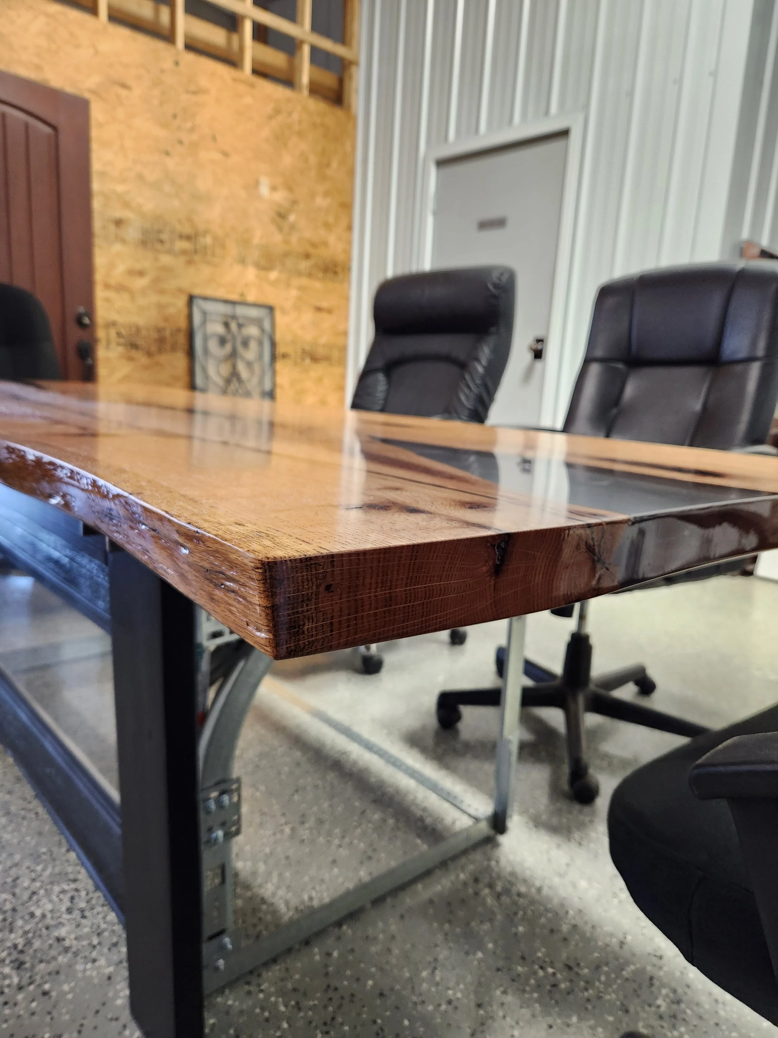Meeting room with live edge oak conference table, black leather chairs, a white door, and metal walls.