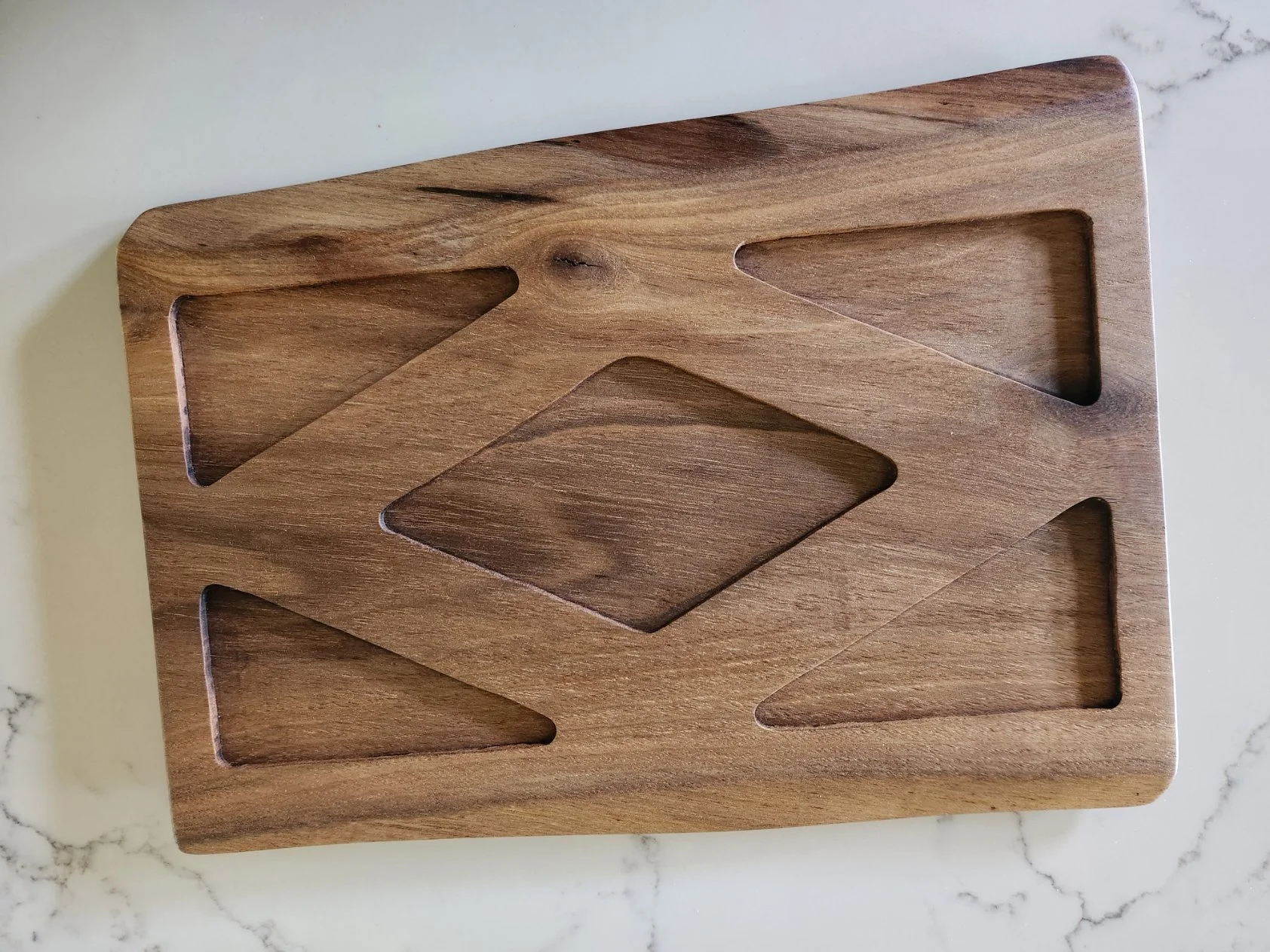A walnut live edge serving tray with multiple butterfly-shaped and one diamond-shaped mold sections, placed on a white marble surface.