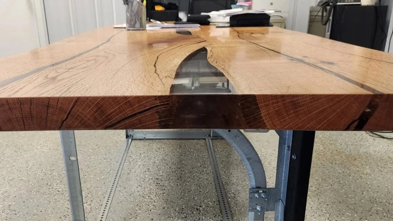A large wooden conference table with a natural edge and a hollowed-out center filled with clear epoxy, supported by metal garage door track styled legs, in a local business.