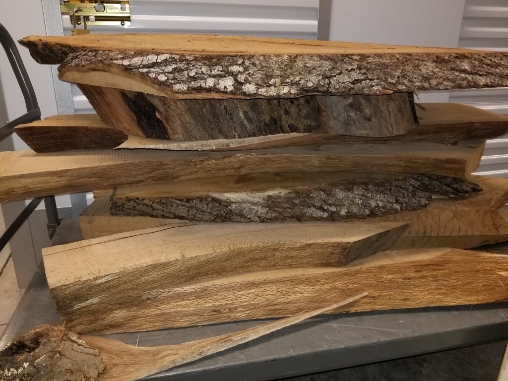 Stacked pieces of rough-cut and sawed wood with bark on some pieces.