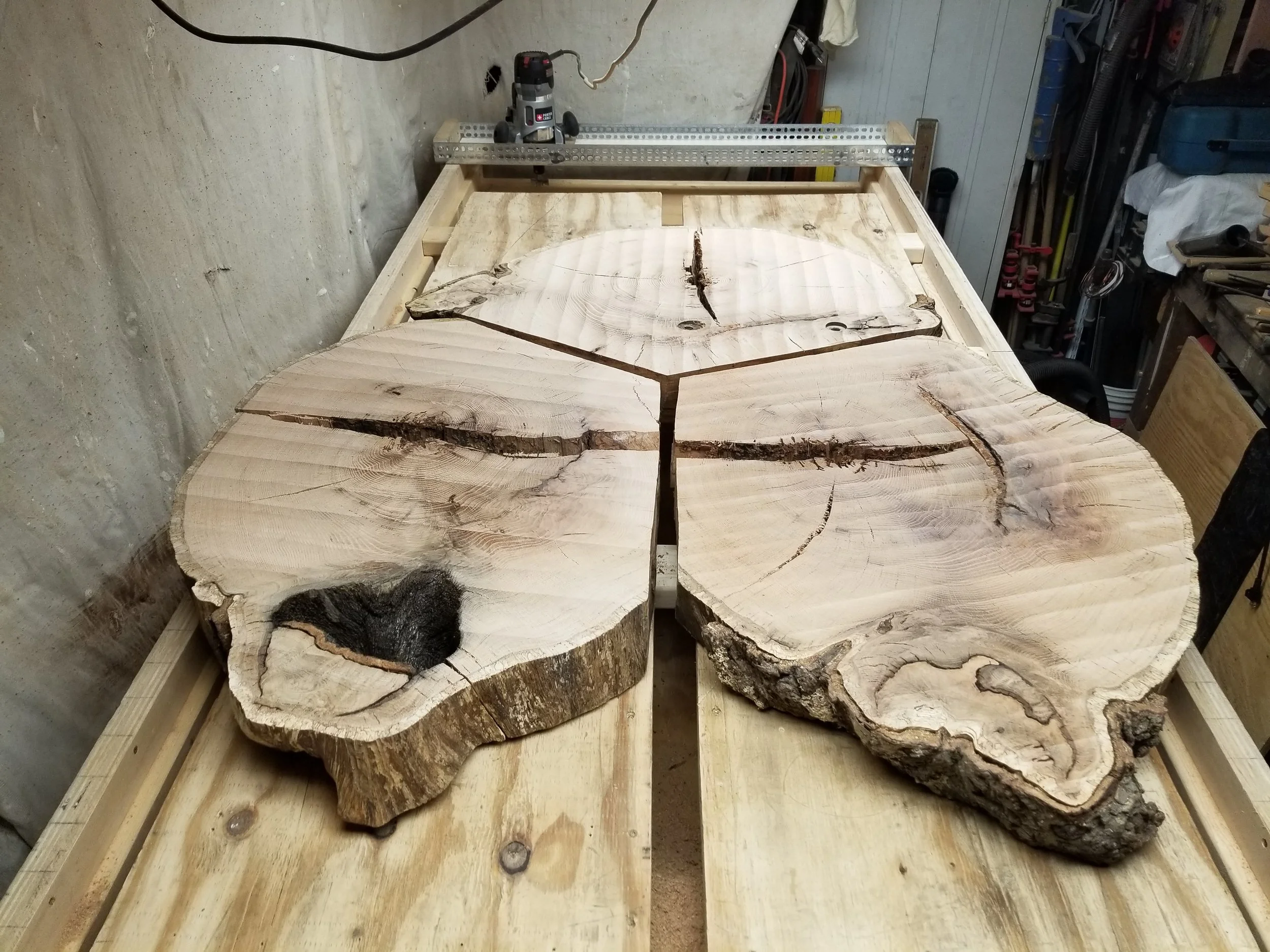 Large wooden slabs with natural edges on a workshop workbench, with tools and workshop items in the background.