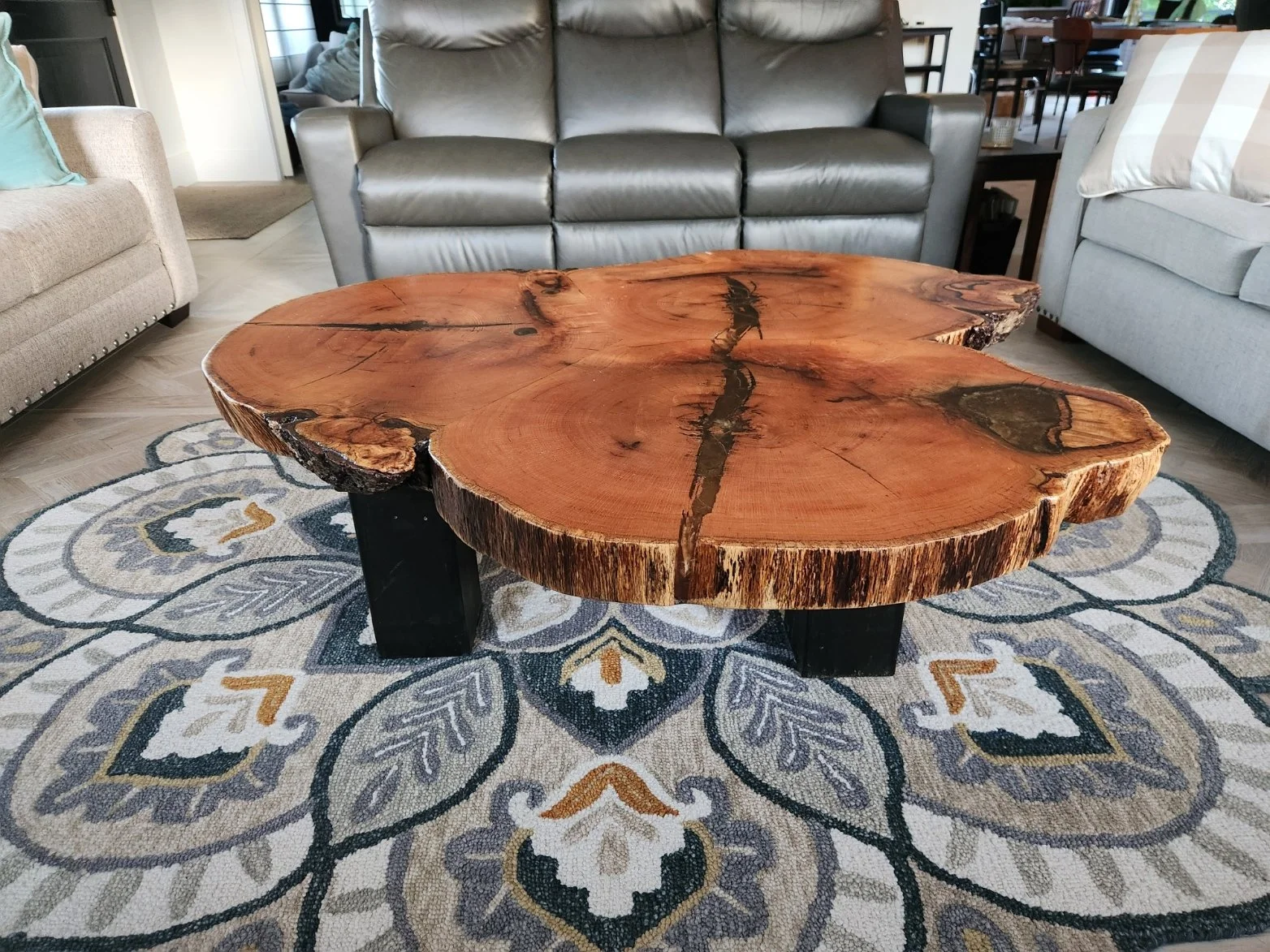 A rustic, natural wood coffee table with a live edge, resting on a decorative area rug in a living room setting.