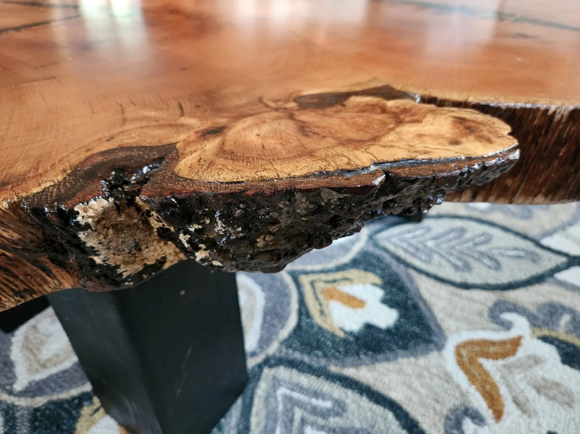 Close-up of a wooden table with a natural edge showing the wood grain and the bark on the side.
