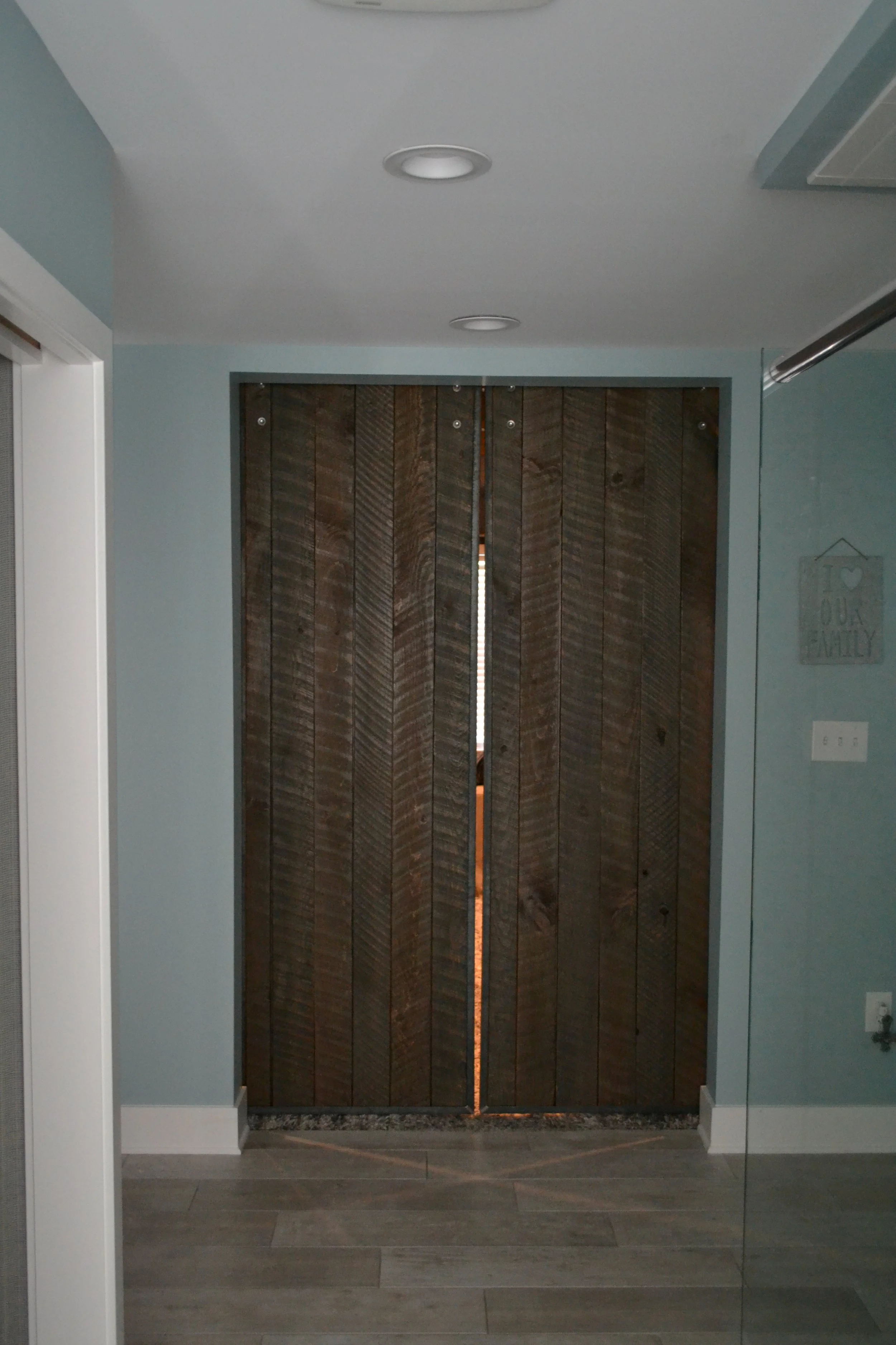 Wooden sliding barn doors in a modern home with light blue walls, ceiling lights, and a tiled floor.