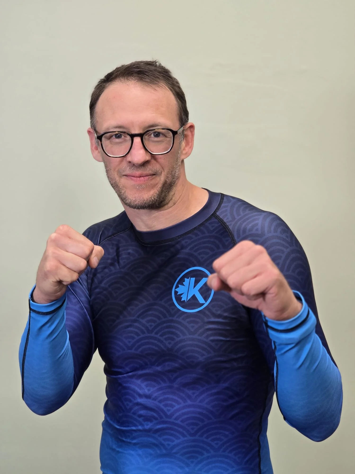 A man wearing glasses and a blue patterned sports shirt, in a fighting stance with fists raised.