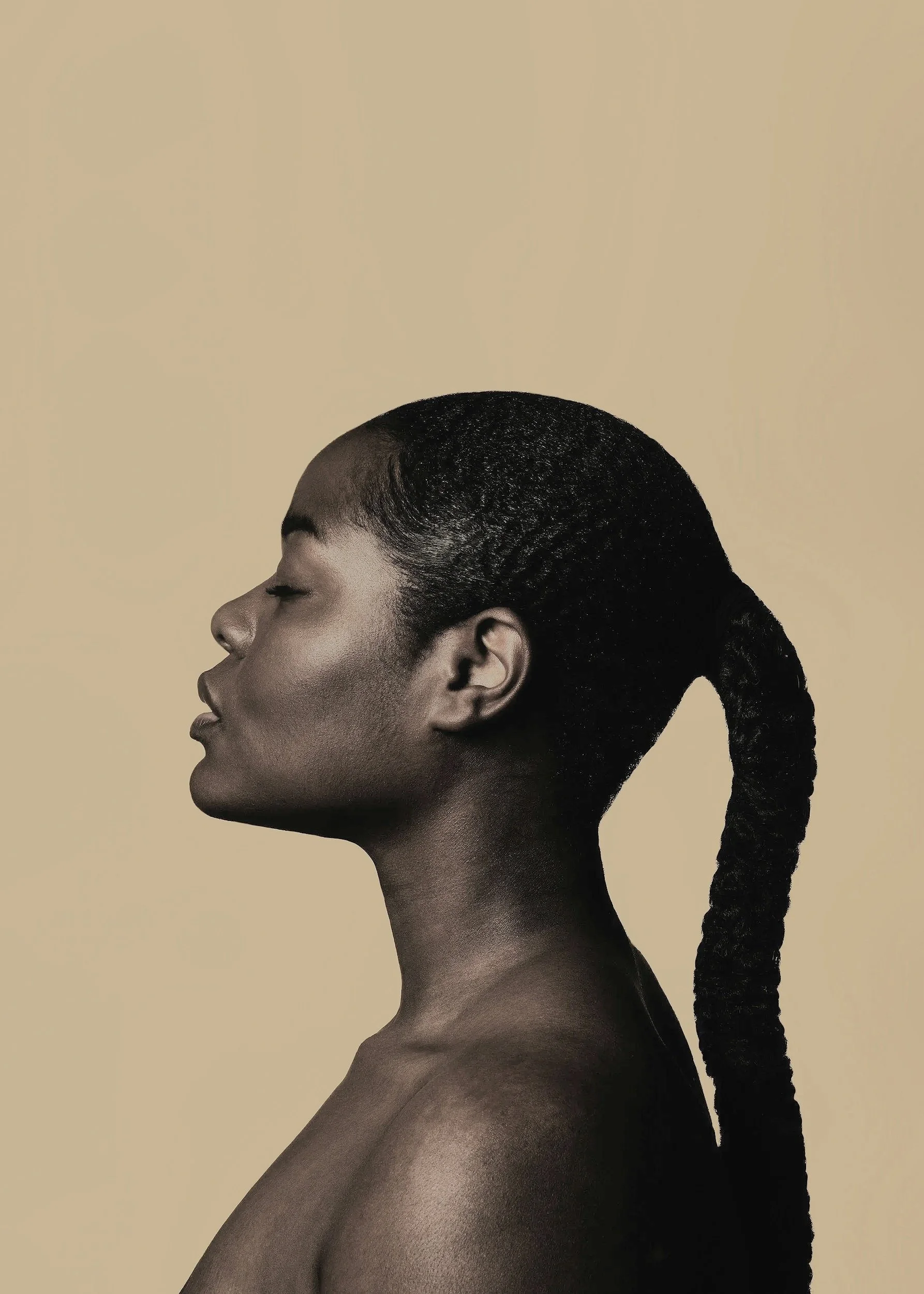 Profile portrait of a Black woman with a long braided ponytail against a beige background