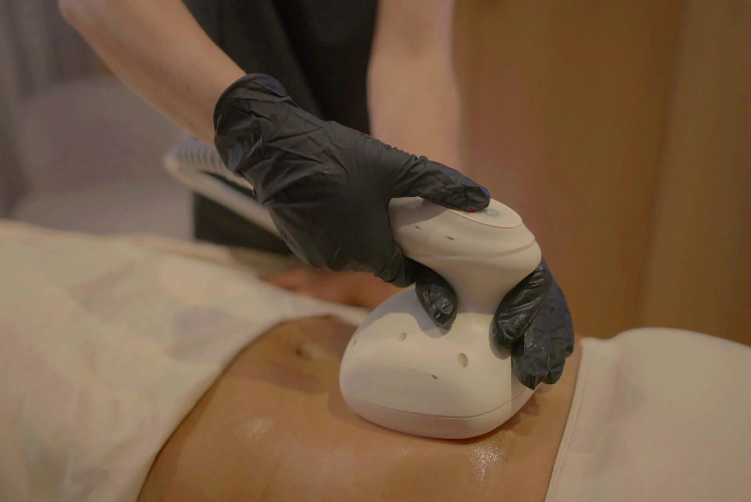 Gloved hands using a white handheld electronic device on a patient's foot during a medical procedure