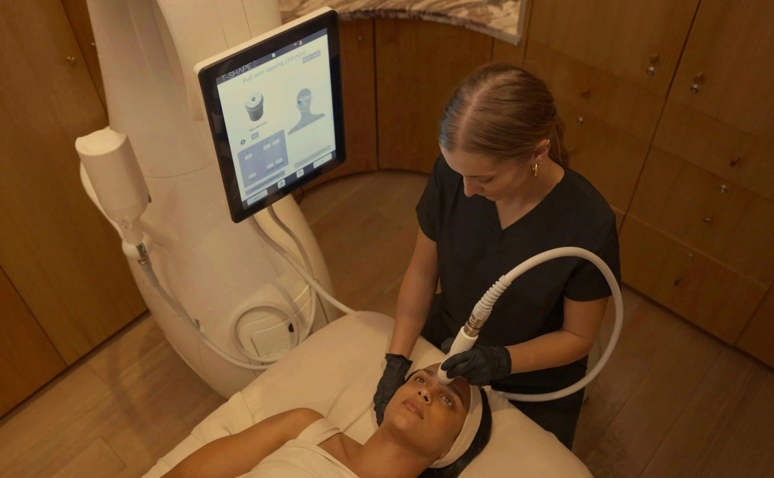 Woman receiving a facial treatment from an aesthetician using a handheld device in a spa treatment room