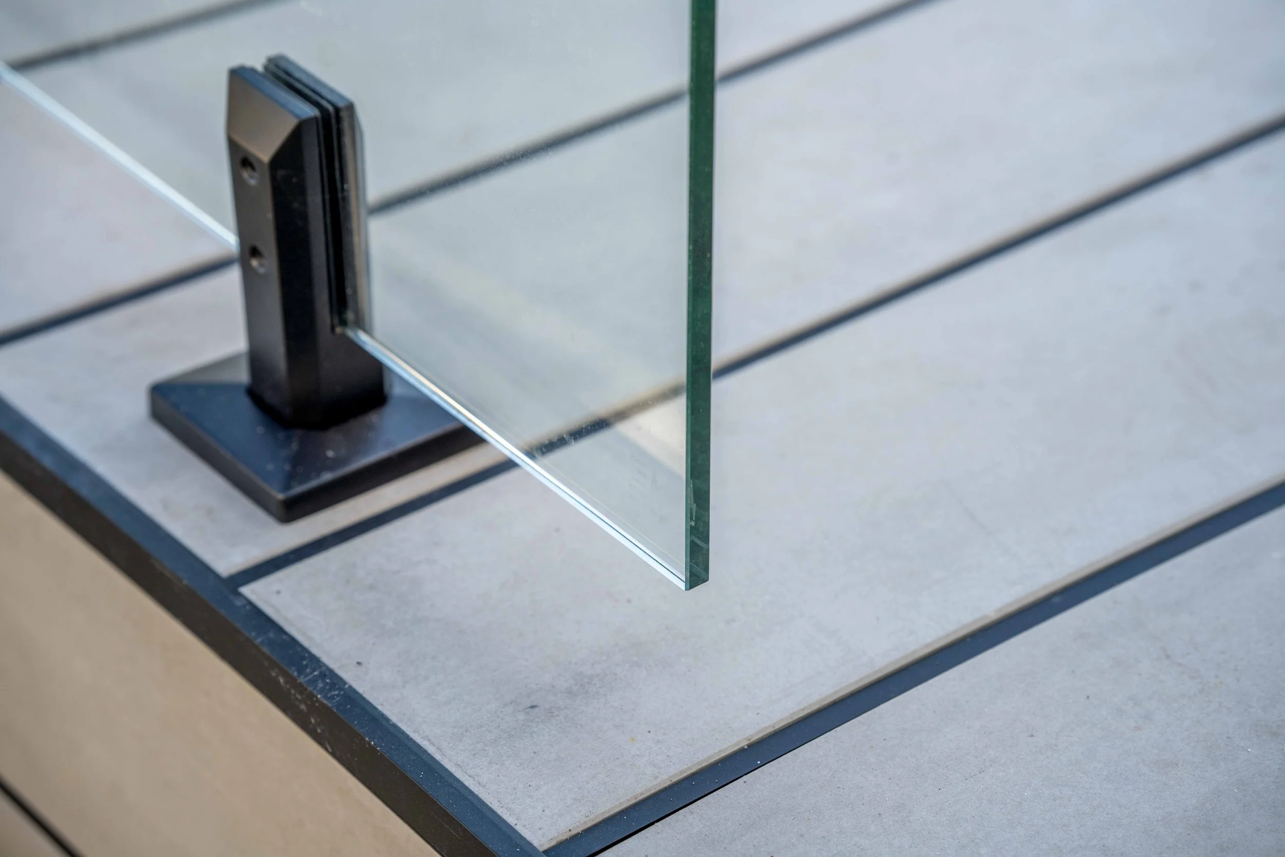 Close-up of a glass panel edge mounted on a metal stand, positioned on a slatted outdoor table.