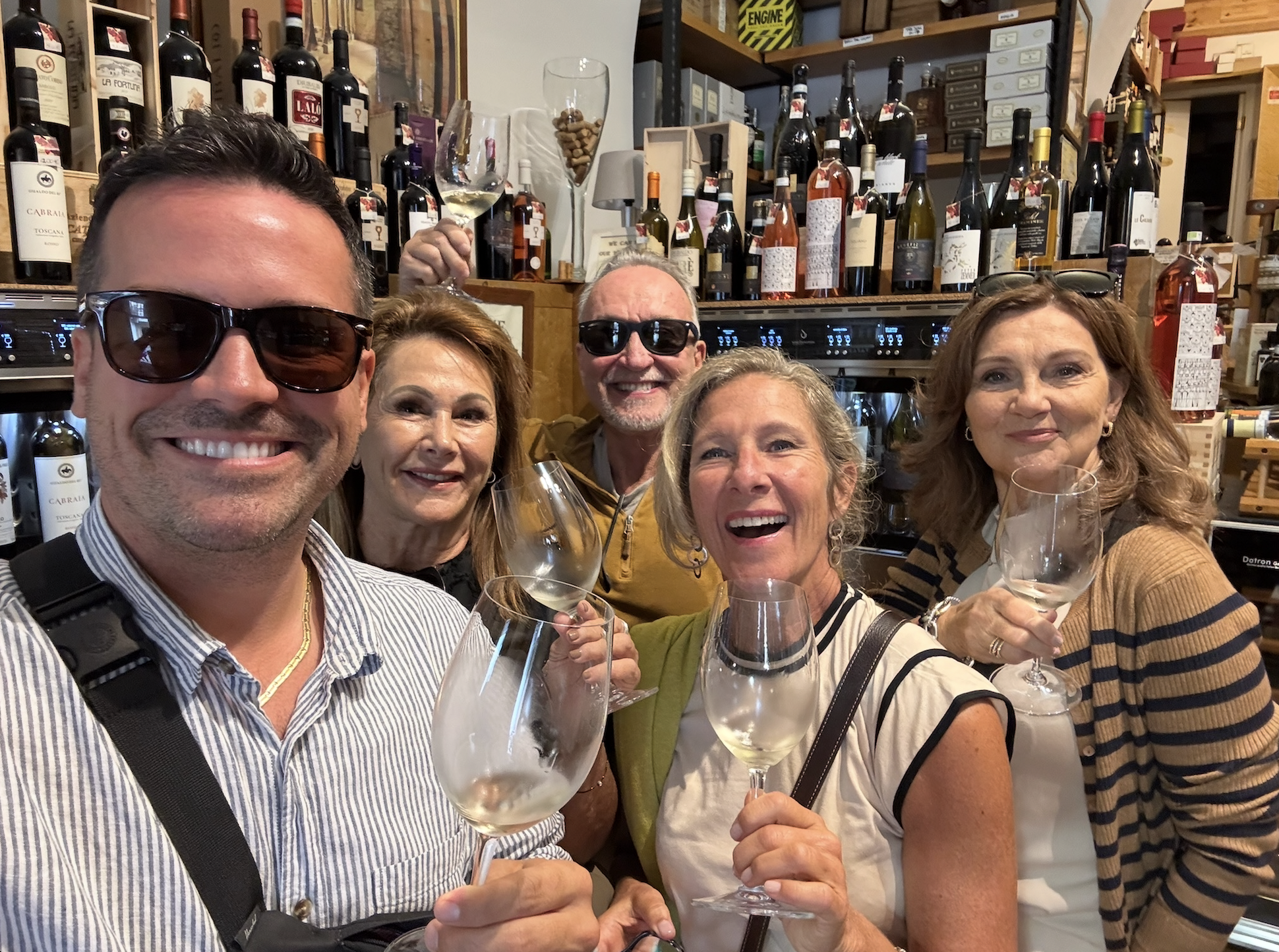 A group of six people smiling and holding wine glasses, chef Ed included, in a wine shop in italy.