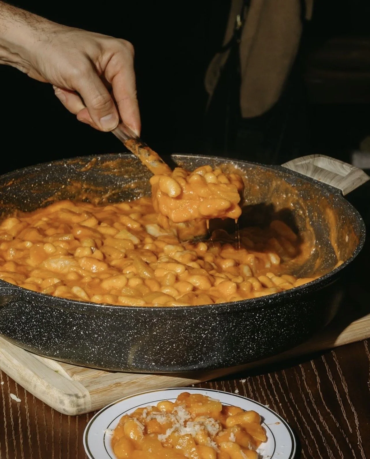 A person serving a plate of baked pasta with cheese from a large pan of macaroni in tomato sauce.