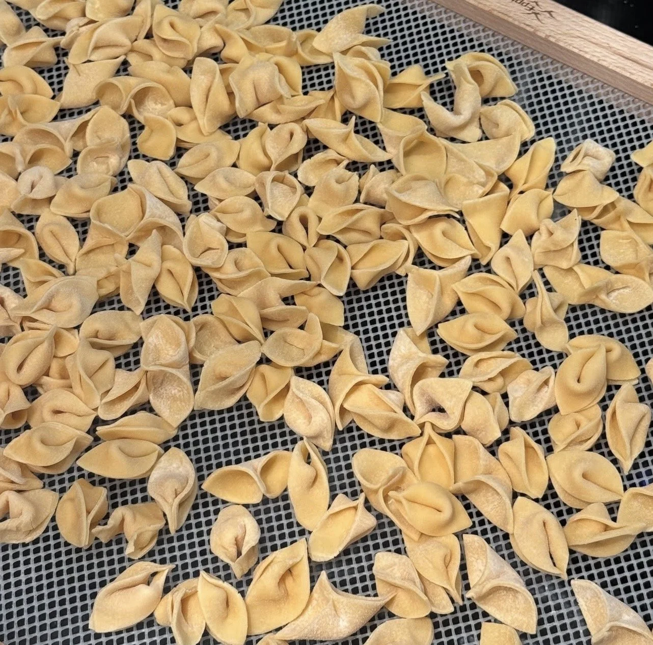 Dried tortellini pasta spread out on a mesh drying rack.