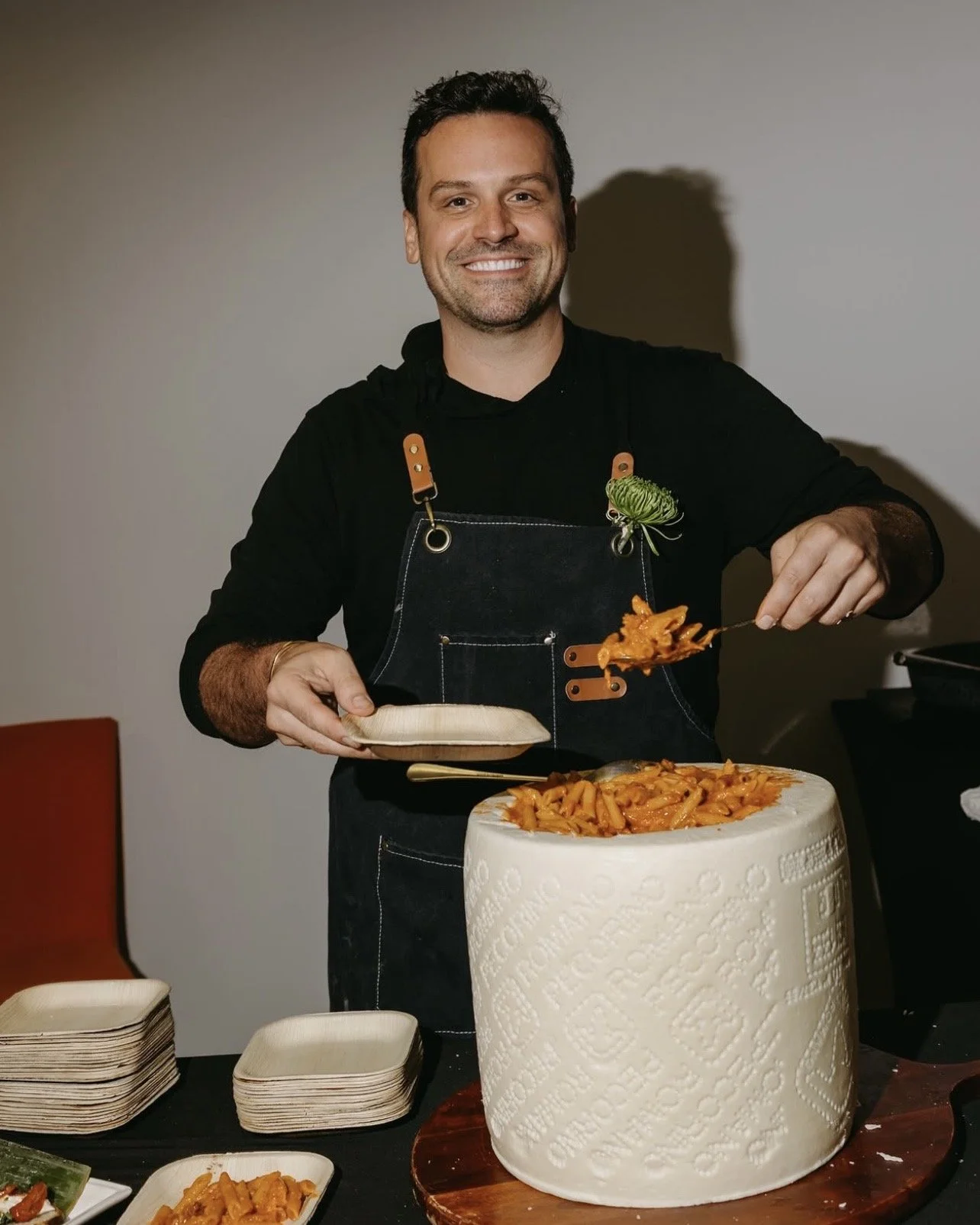 Chef Ed smiling while scooping pasta on a plate from a large cheese wheel used as serving platter.