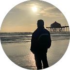 Person standing on the beach at sunset near a pier.