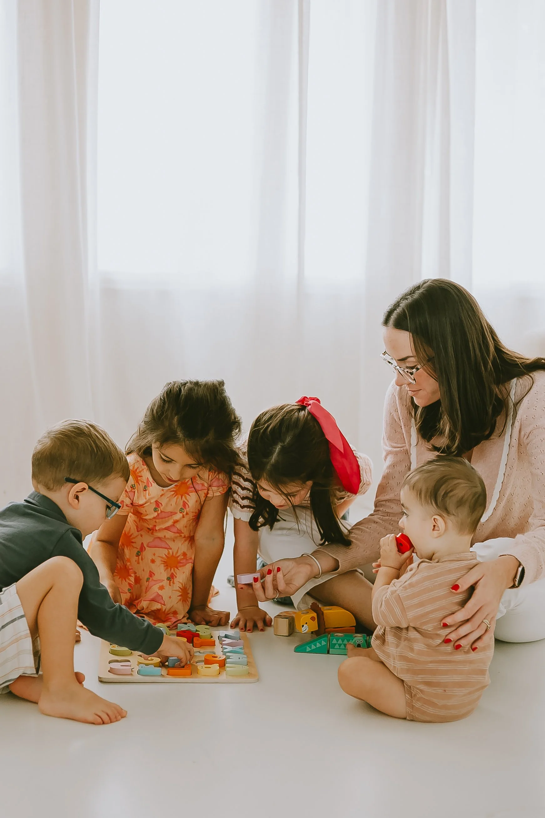 A group of children and a woman sitting on the floor playing with colorful educational toys and books.