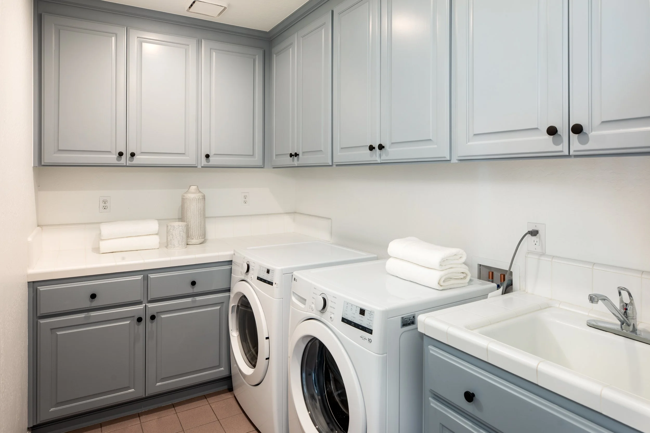A laundry room with light gray cabinets, white countertops, a washer and dryer, and neatly folded white towels on the counter.