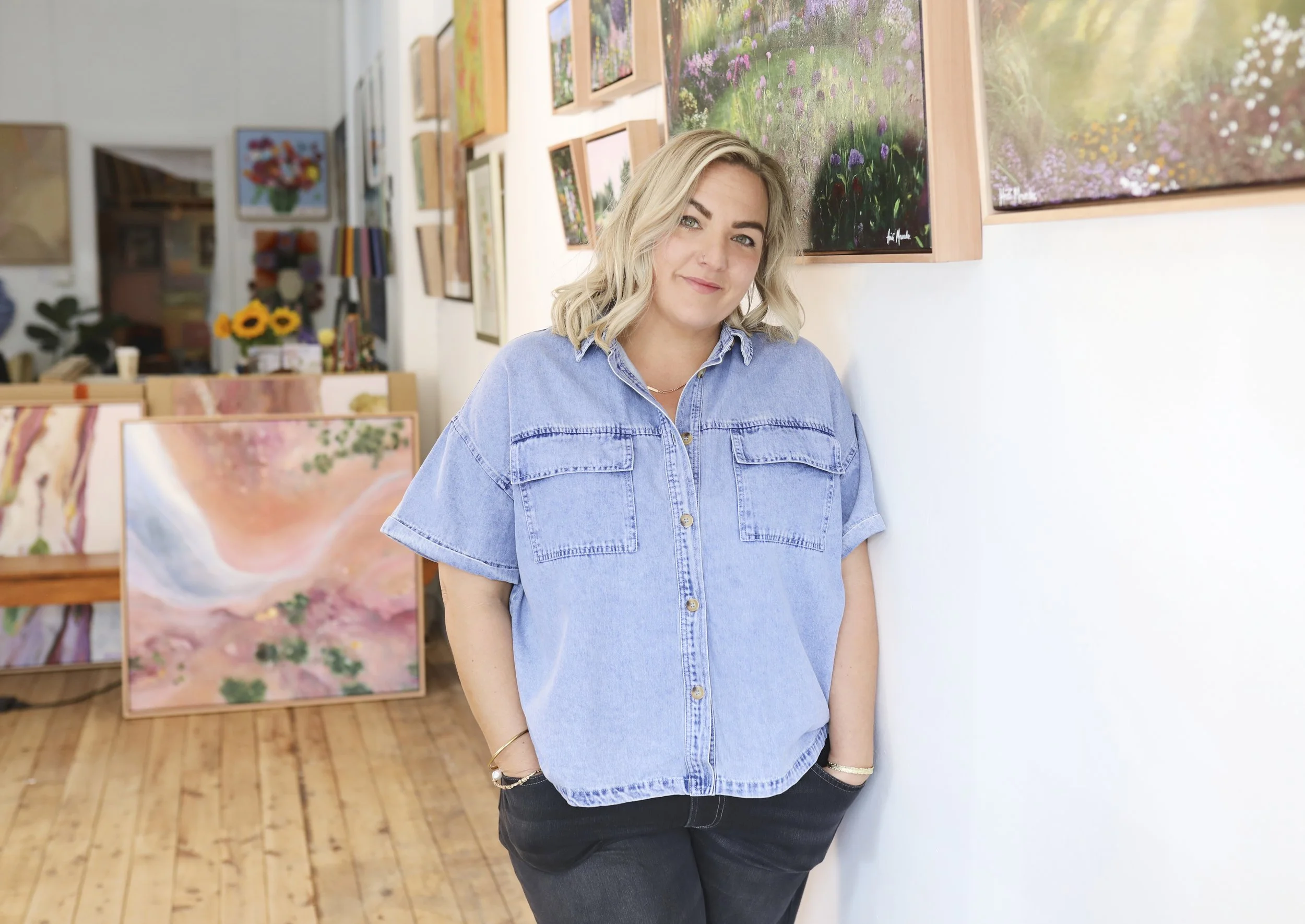 Heidi Maunder, standing in an art gallery with her original colourful paintings on the walls.