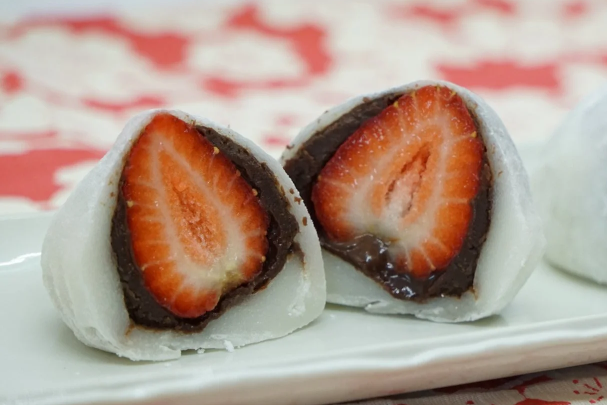 A mochi dessert with a fresh strawberry center and chocolate filling, cut in half to show the inside.
