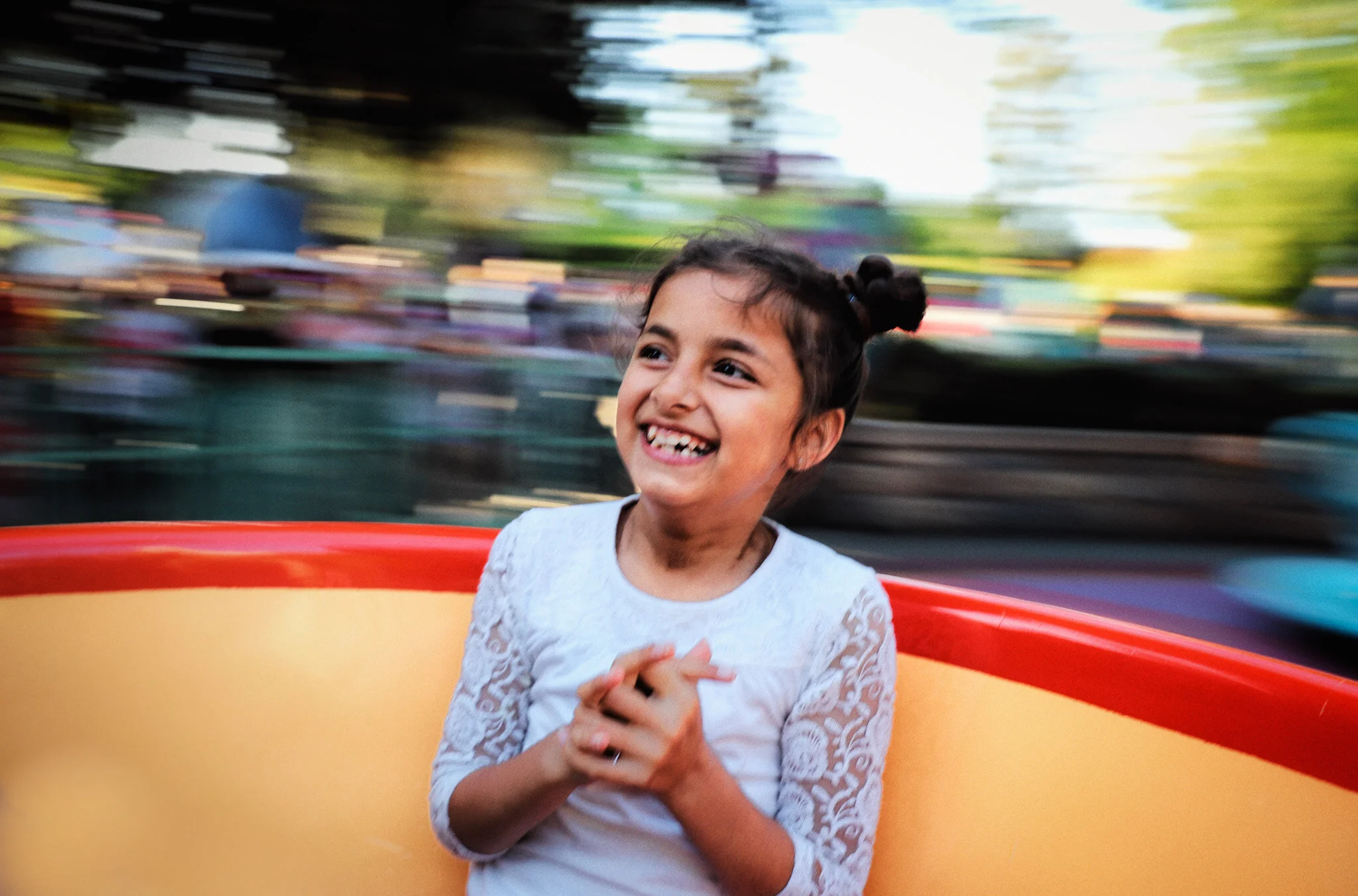 A young girl smiling happily as she rides a spinning amusement park ride with colorful blurred background.