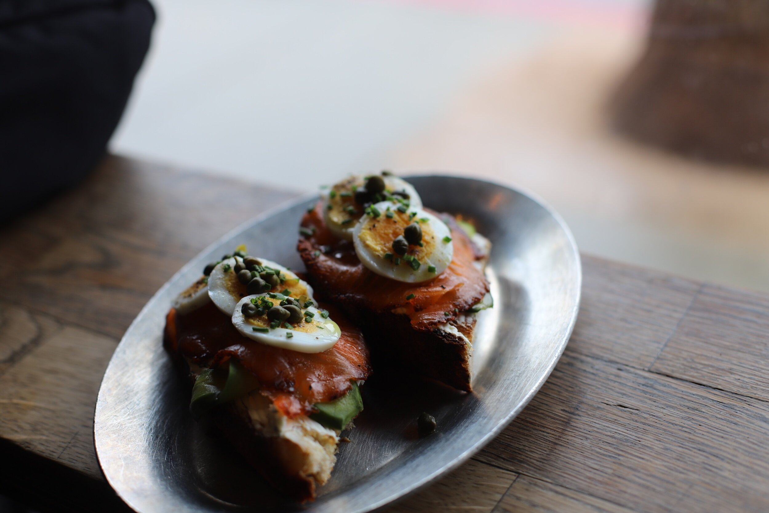 Open-faced sandwich on a silver platter with smoked salmon, halved boiled eggs topped with chopped herbs and capers.