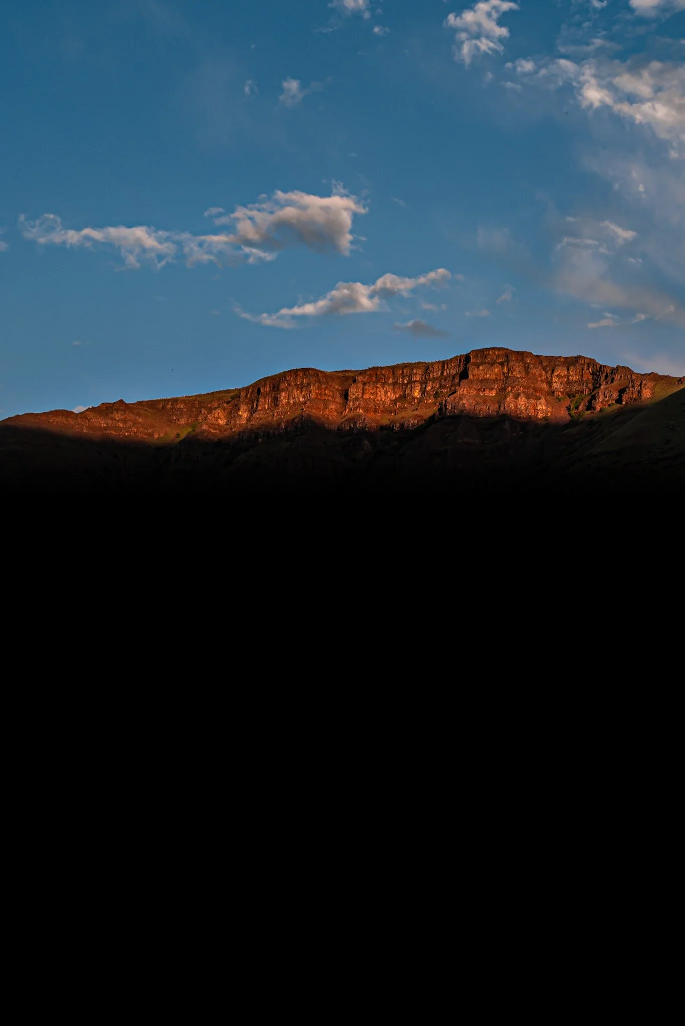 Sunset or sunrise over a rocky mountain ridge with a partly cloudy sky.