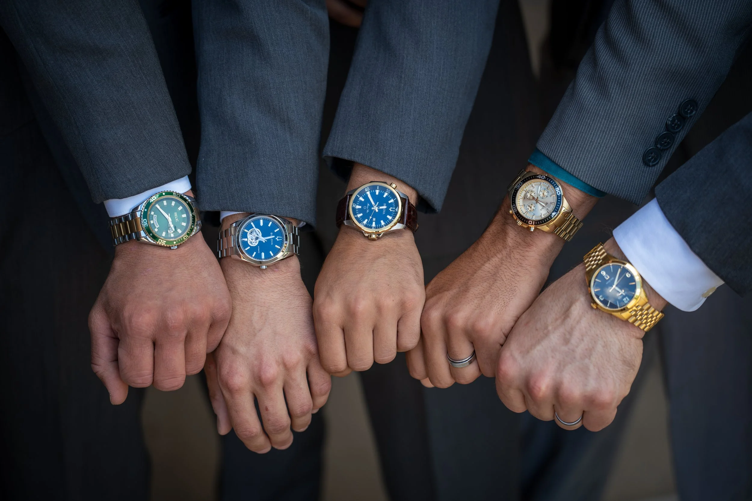 Multiple individuals showing their wrists with diverse watches, dressed in formal suits and shirts.