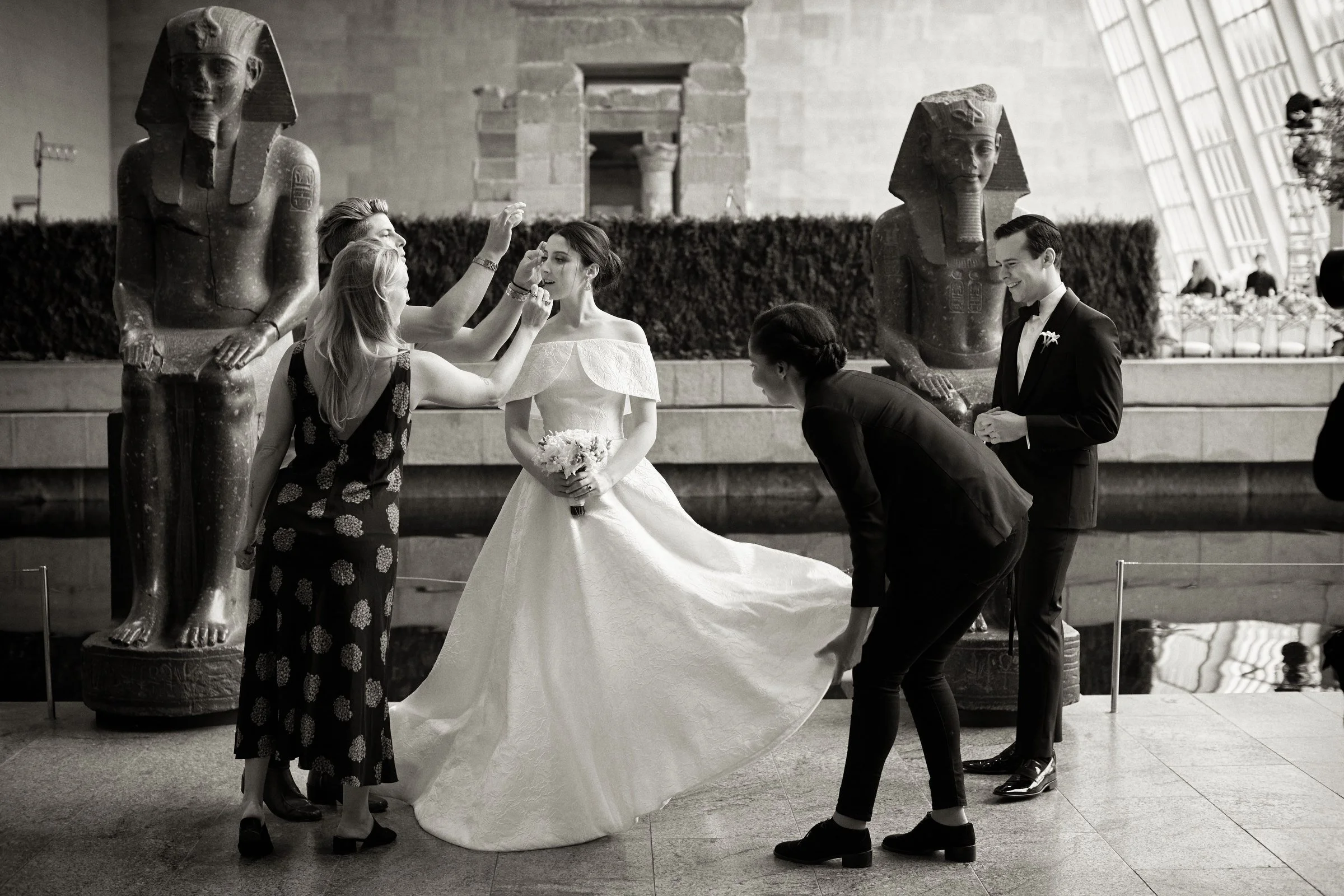People getting ready for a wedding ceremony inside an airport terminal, with two statues of Egyptian figures in the background.