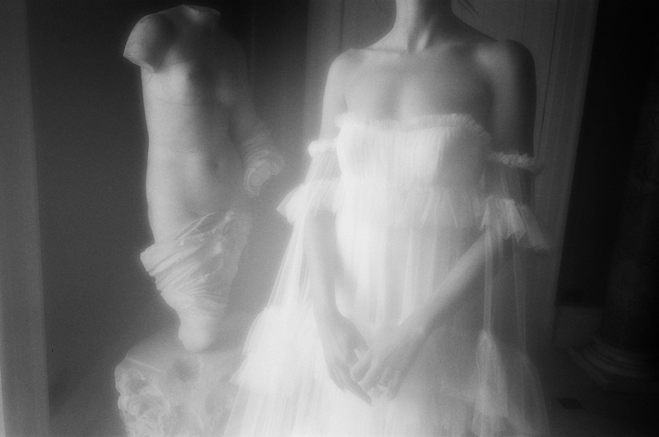 A black and white photograph of a woman in a strapless dress posing with her hand on her hip. The image has a vintage appearance.